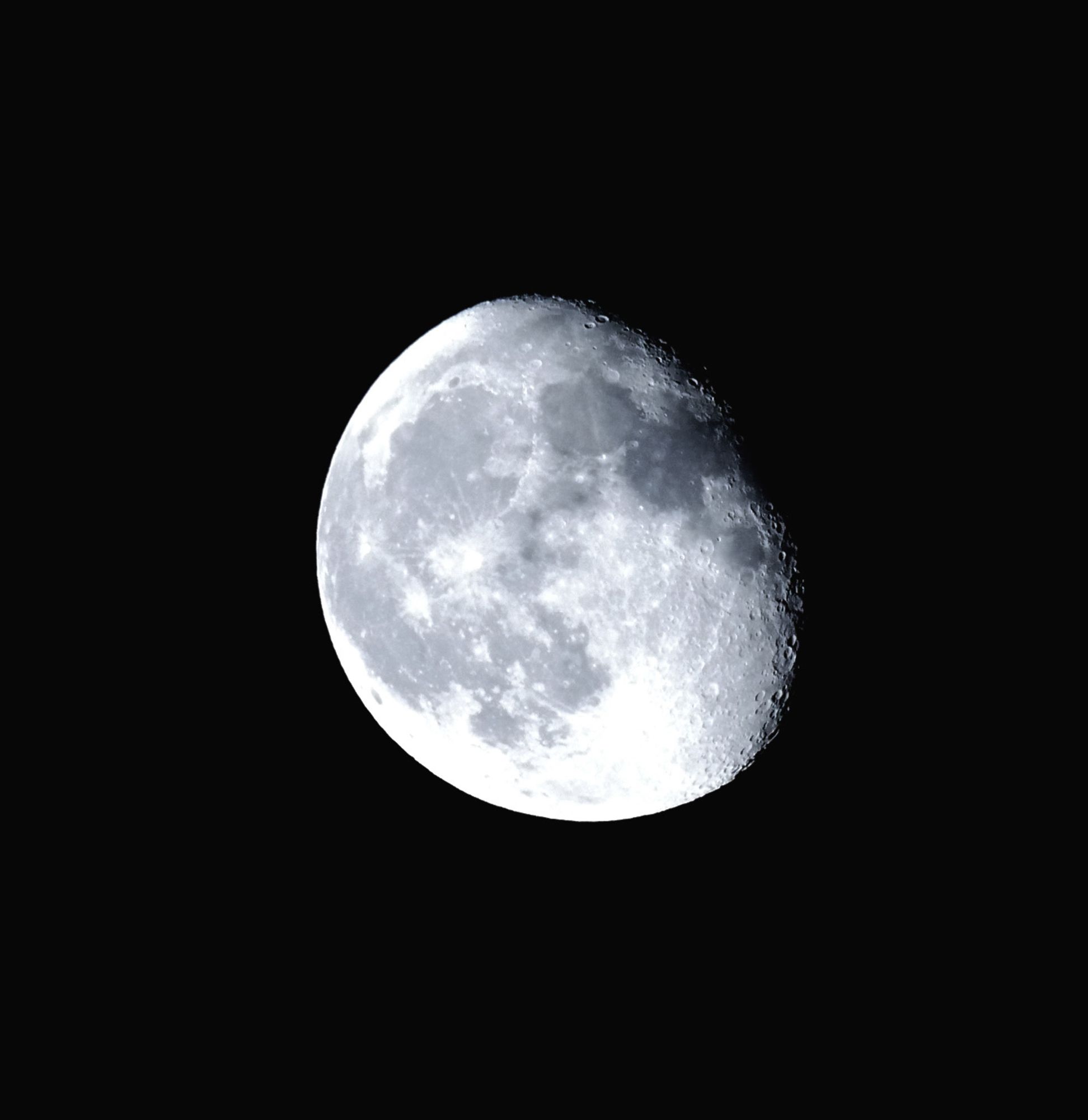 Photo de la lune gibbeuse décroissante, dans les tons de gris bleuté. On voit le relief des cratères sur le côté droit.