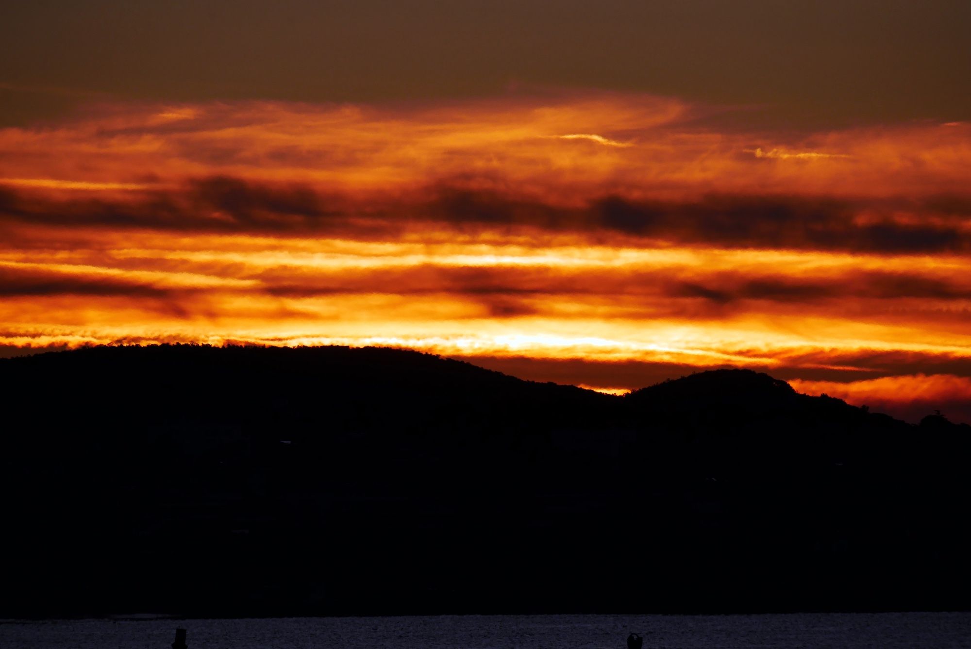 Photo d’une bande de nuages éclairés de rouge et or par les rayons du soleil se levant derrière des collines.