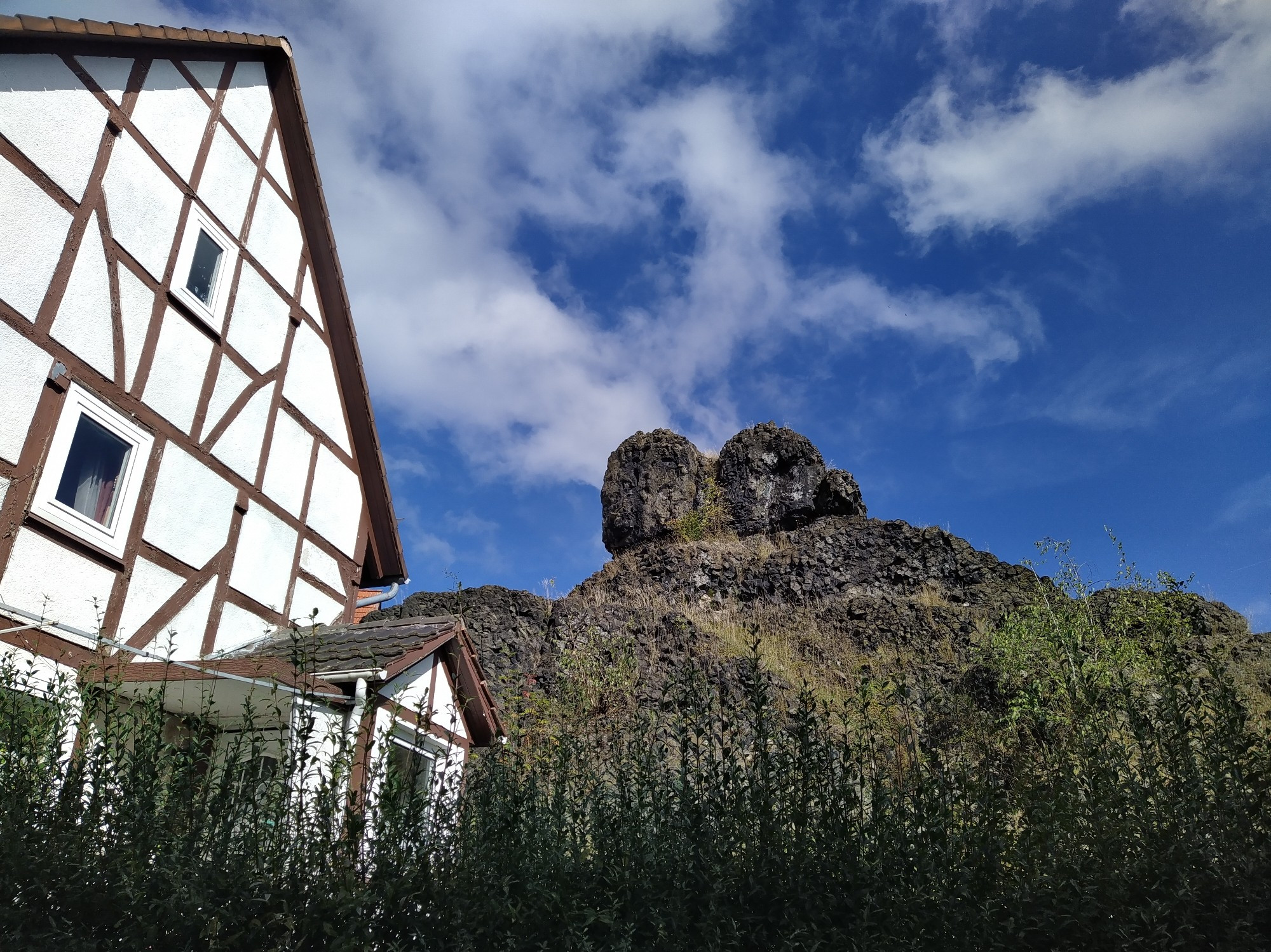 Blick an einem Fachwerk Haus vorbei auf das Haus überragende Felsen