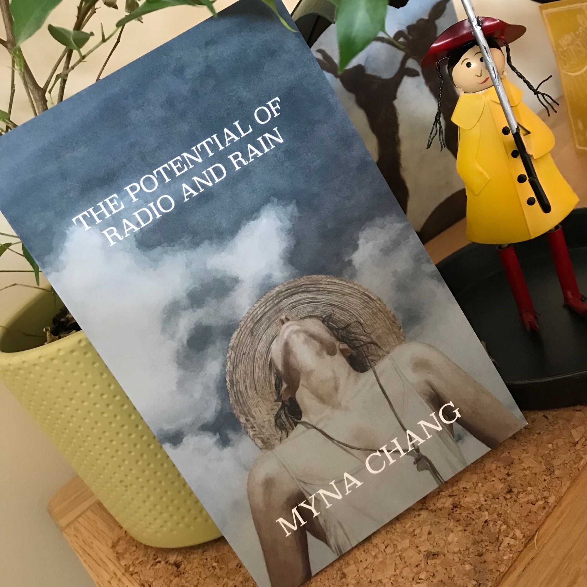 A copy of Myna Chang’s “The Potential of Radio and Rain”; the front cover shows a woman in a straw hat looking up at the sky.