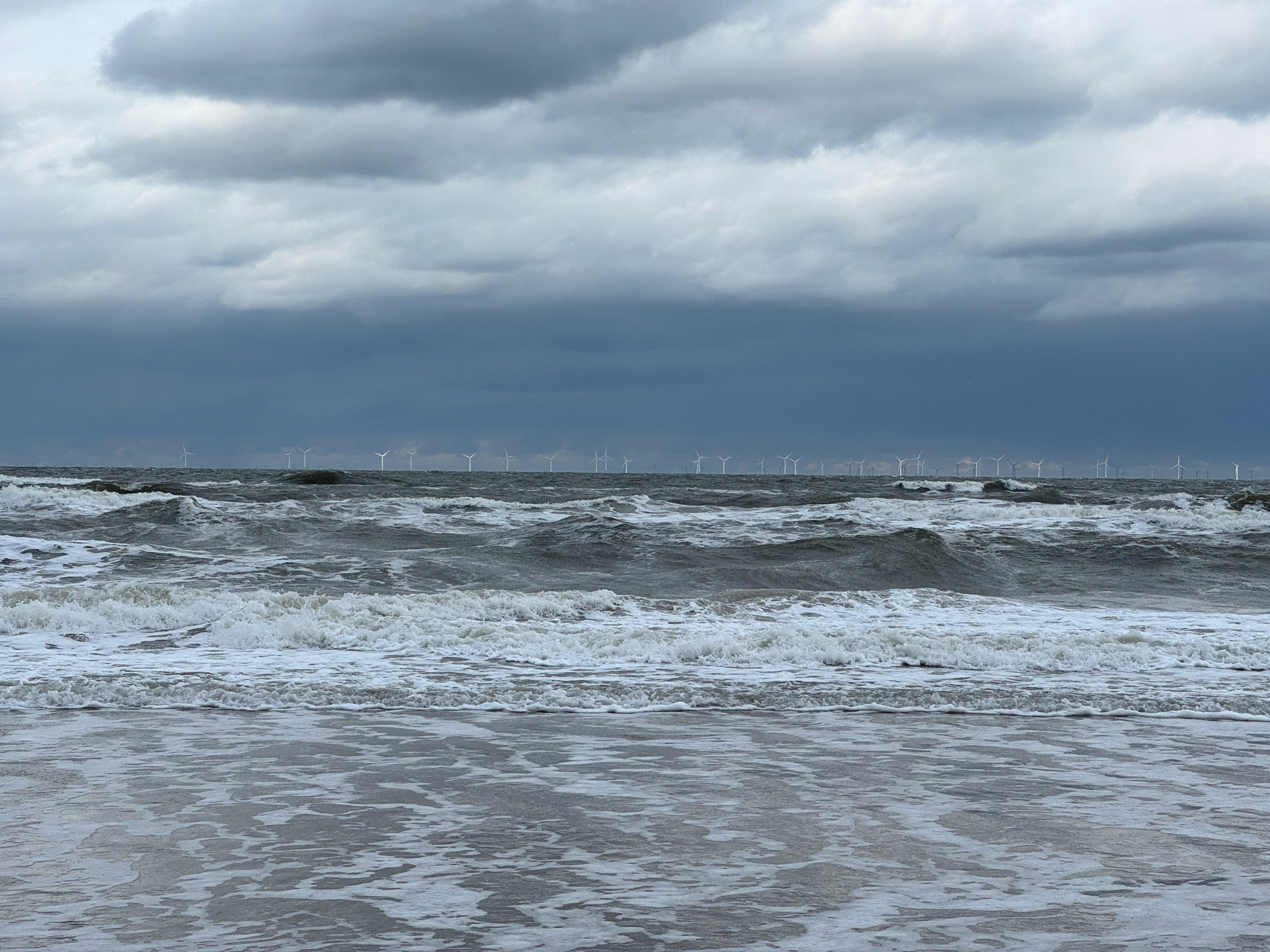 A rough sea under dark clouds, with windmills on the horizon.