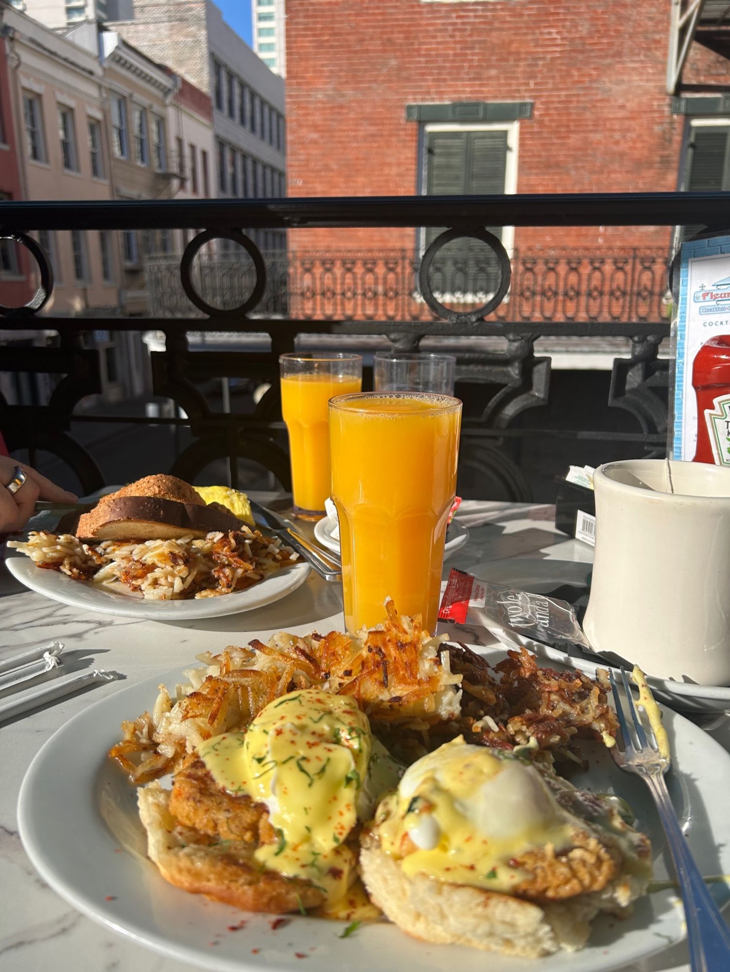 Two breakfast plates and cups of orange juice on a balcony table overlooking the street