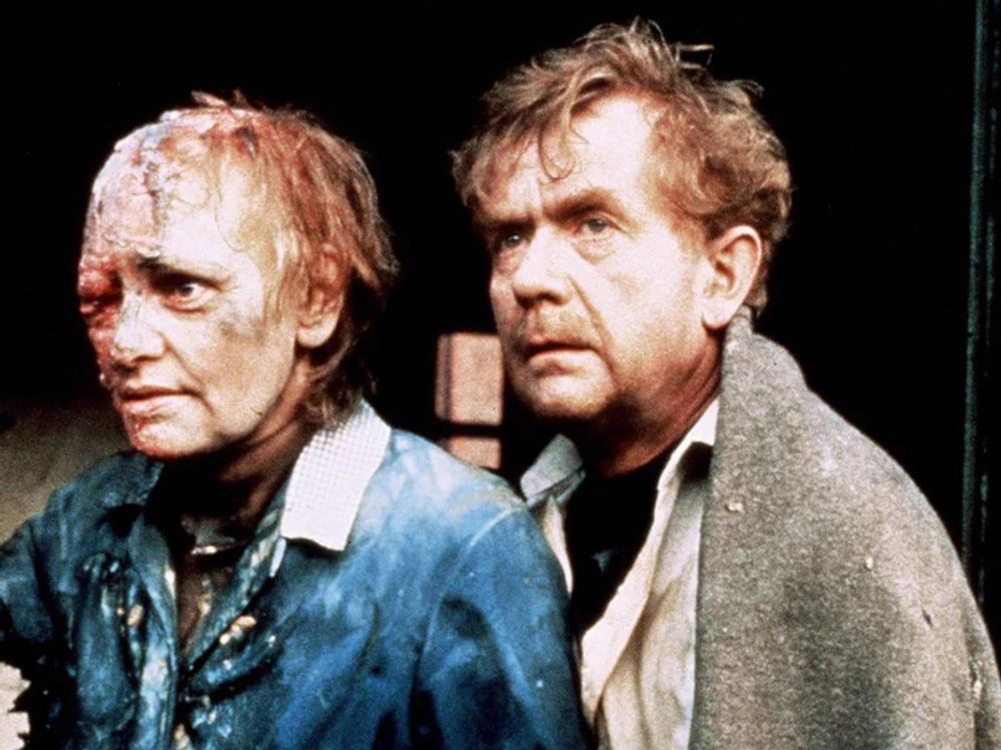 A publicity still from "Threads" showing and older man and woman. Her head is badly burned and partially melted and she has lost much of her hair. The man looks visibly uninjured but concerned.