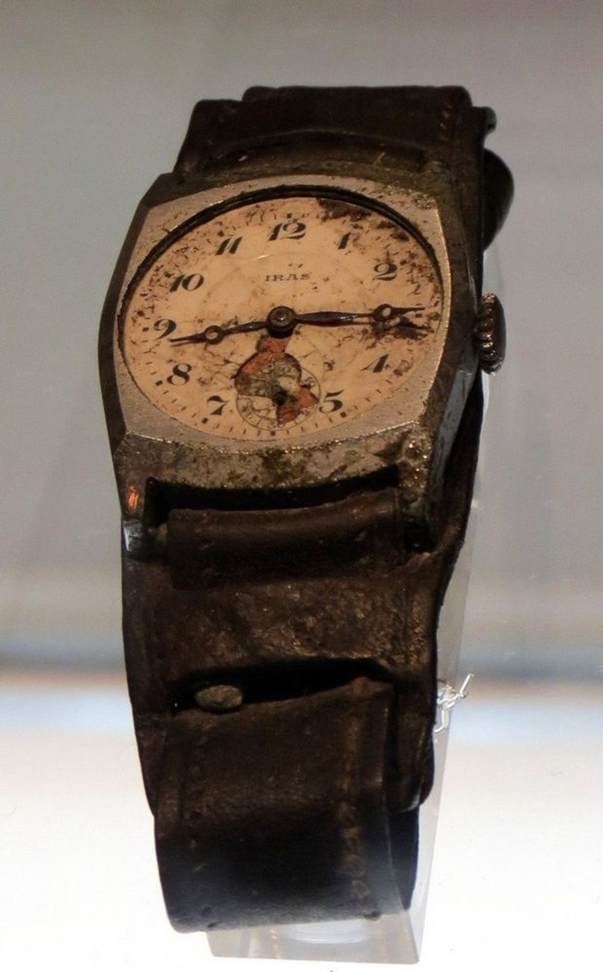 A color photograph of a damaged wristwatch in the Hiroshima Peace Memorial Museum, its hands frozen at 8:15am.