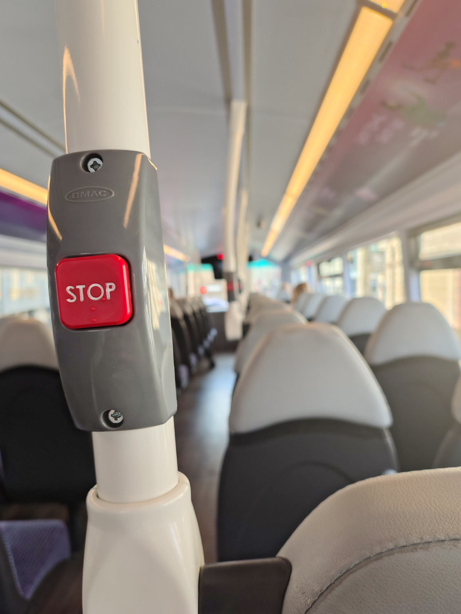 Top deck of an almost empty bus photographed from the back seats, the rwd stop button is the focus of the picture as it gets increasingly soft focus going forwards.