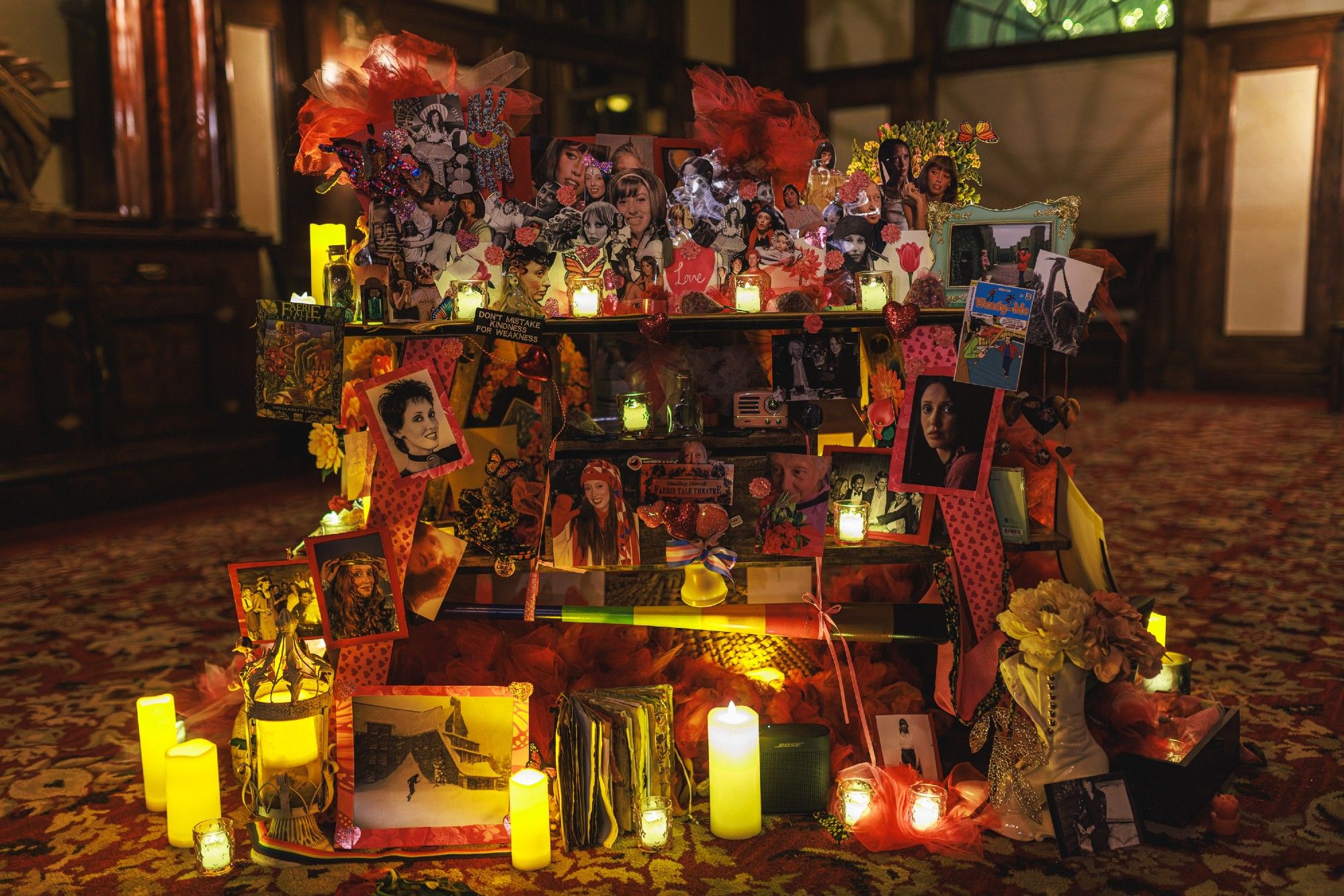 A photo of an altar consisting of many printed pictures of Shelley Duvall and small LED candles and other random items arranged on shelves.