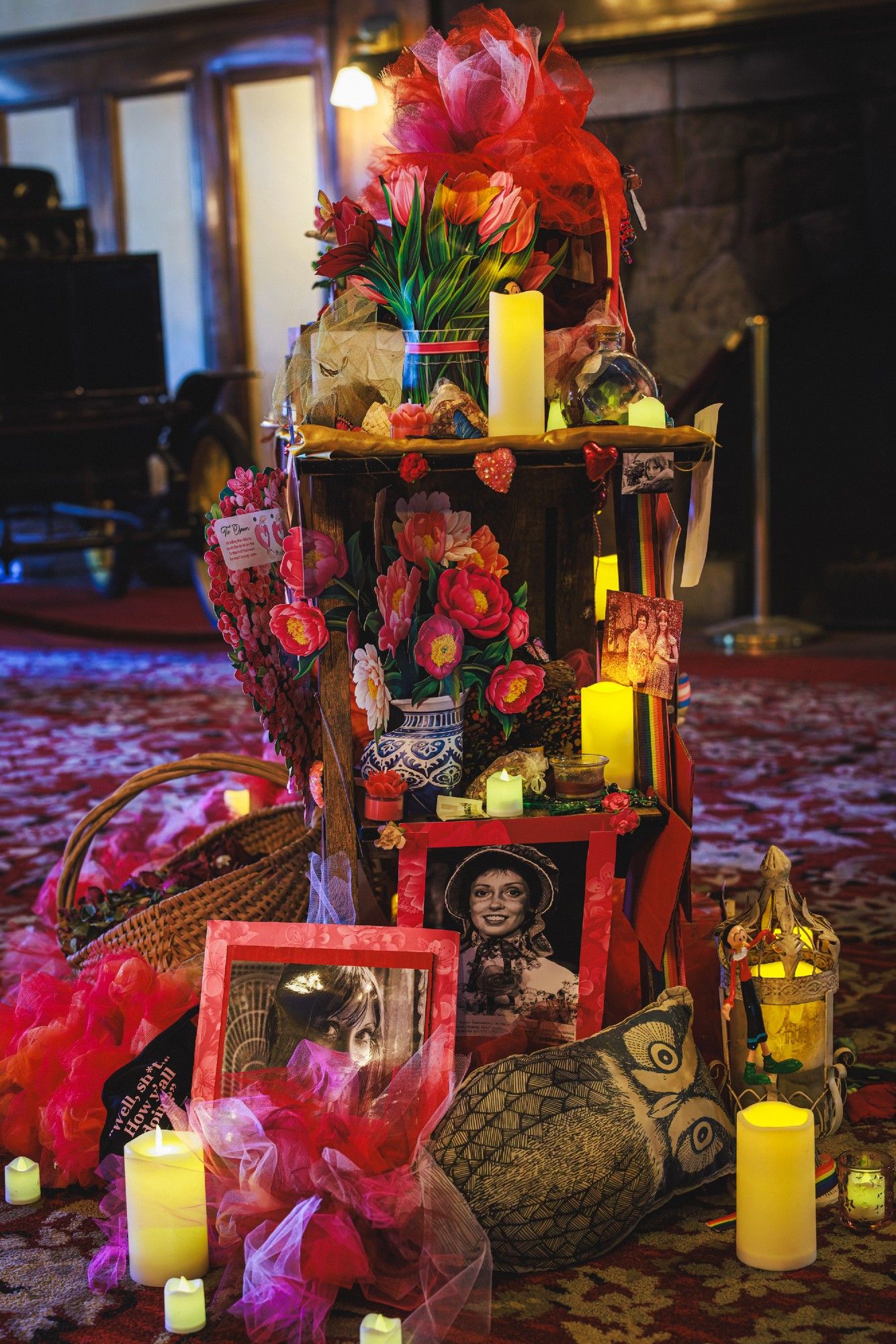 A photo of an altar consisting of many printed pictures of Shelley Duvall and small LED candles and other random items arranged on shelves.