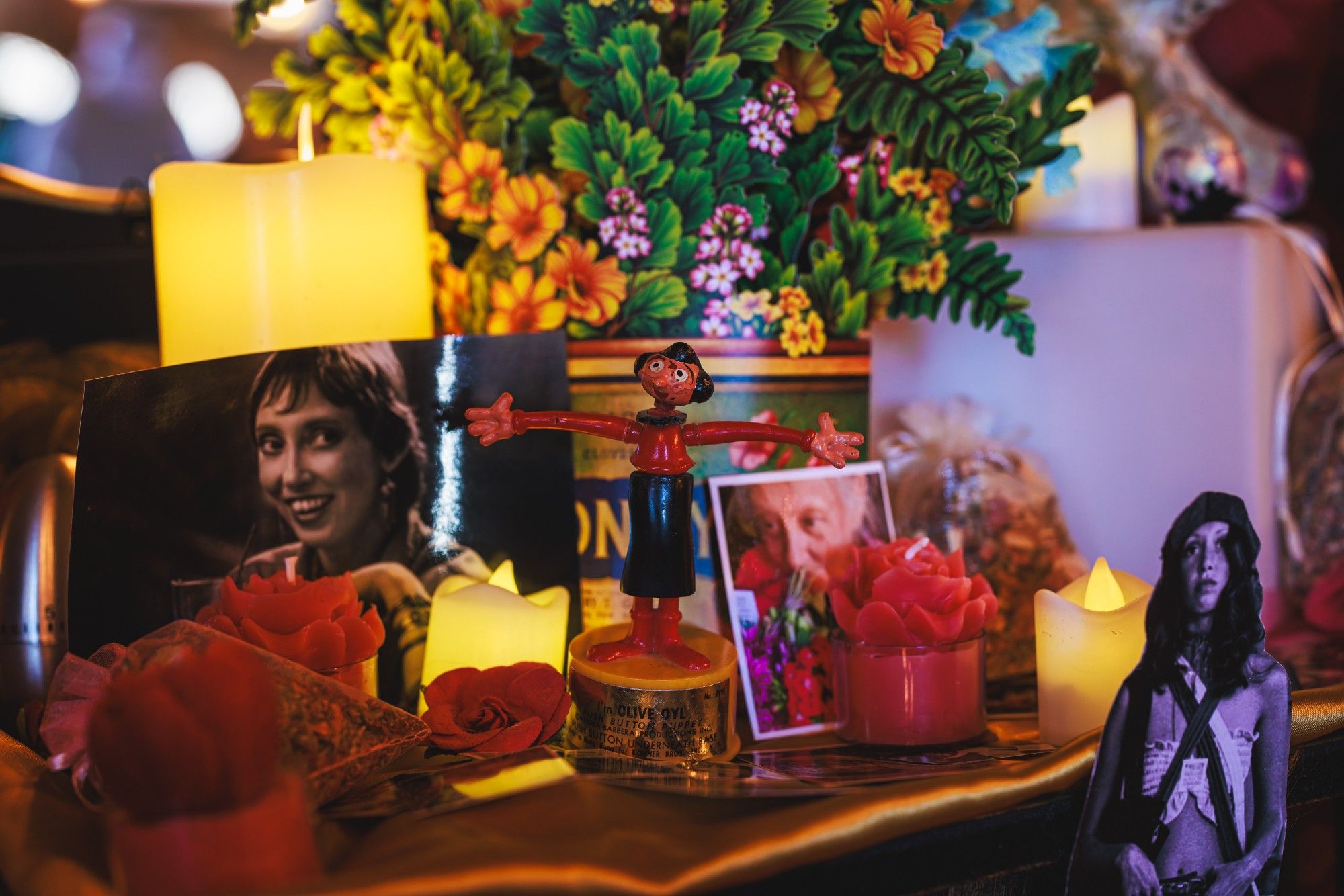 A photo of an altar consisting of many printed pictures of Shelley Duvall and small LED candles and other random items arranged on shelves.