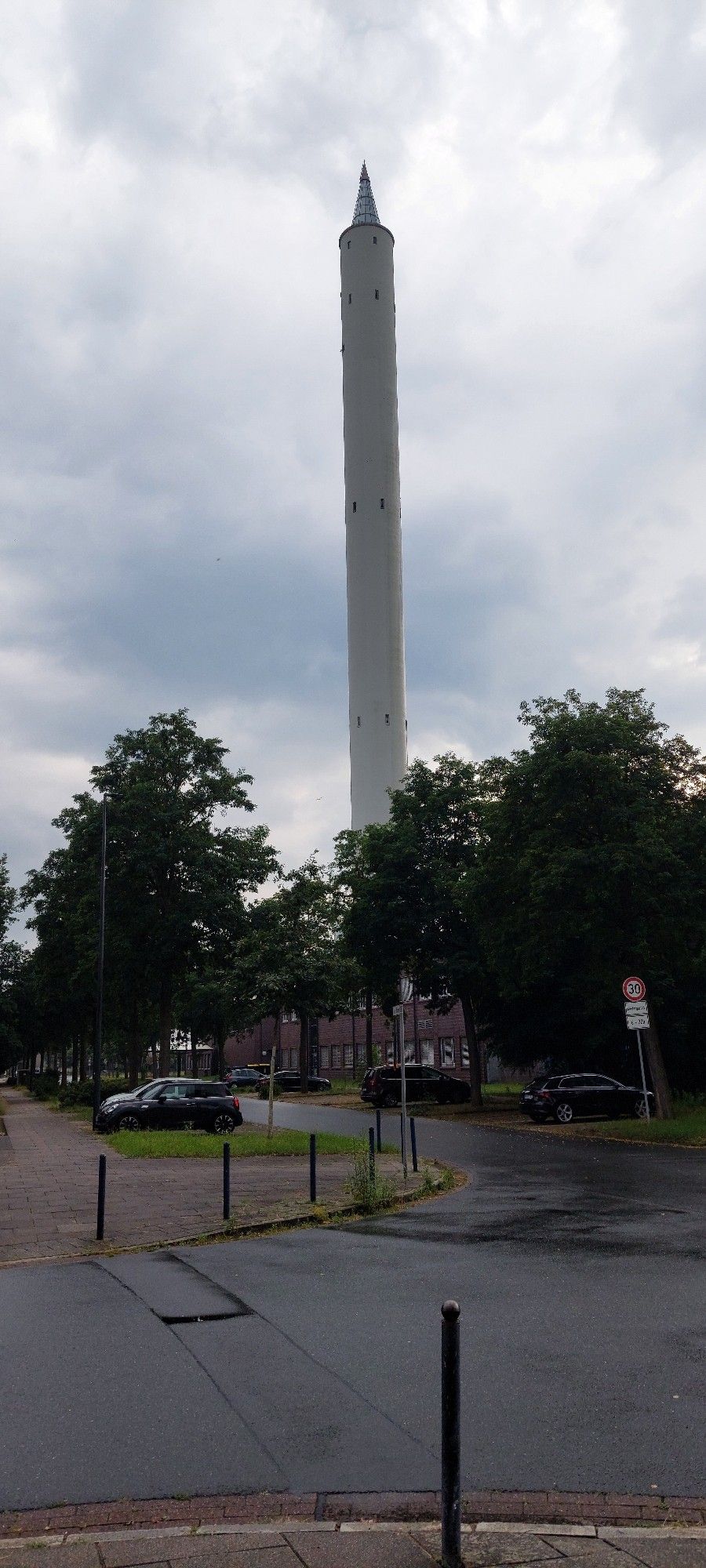 Ein schlanker hoher und weißer Turm vor bewölktem Himmel. Ganz oben eine Spitze aus Glas, die Facetten aus vielen verspiegelten Scheiben hat.