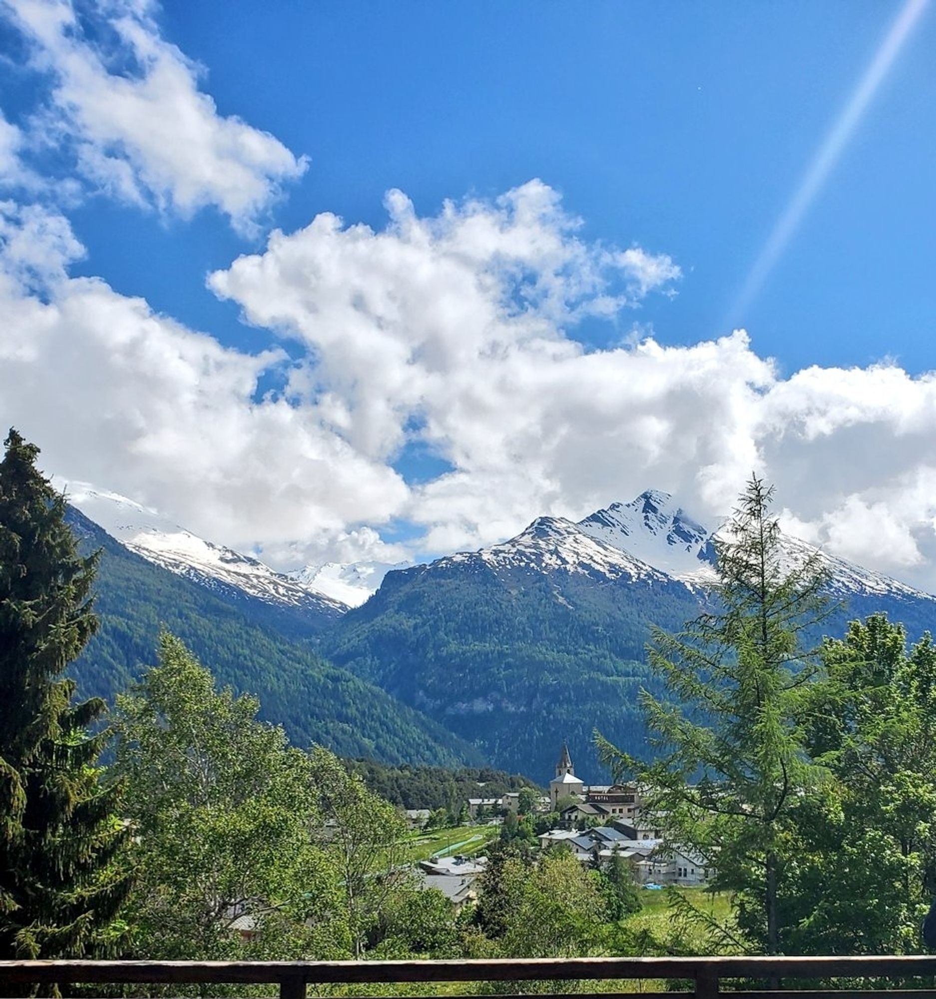 Vue sur un village à clocher et sommets
enneigés, dans une vallée verte