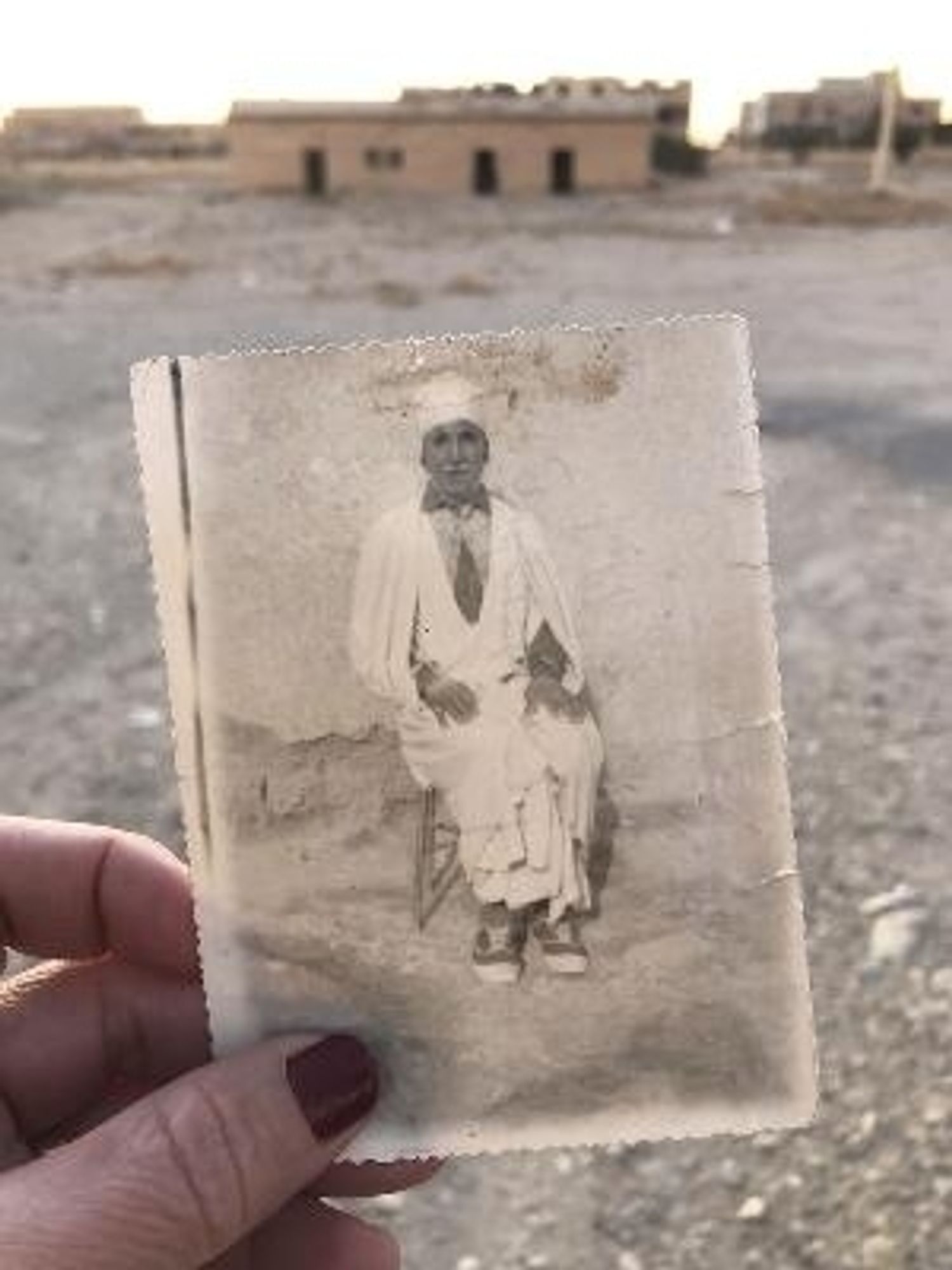 Photographie du grand-père de Dalila Mahdjoub sur arriere-plan de terrain vague, vraisemblablement des restes d'un camp de regroupement