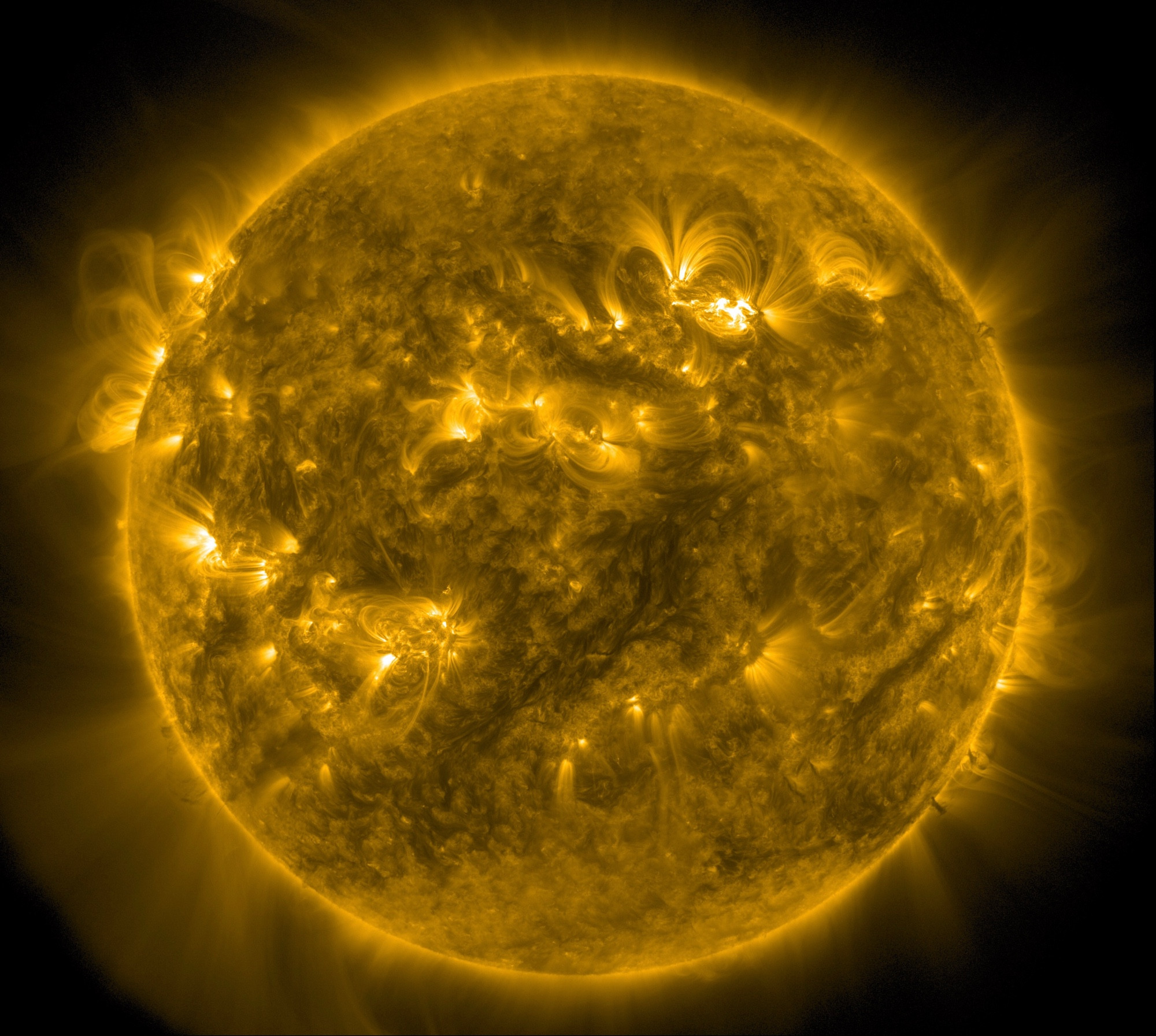 Die ganze erdzugewandte Seite der Sonne in gelber Farbe. In der Mitte mehrere heller dargestellte Aktive Regionen und auch links oben am Rand ein solches Gebiet, von dem Strahlen weit ins All ausgehen.