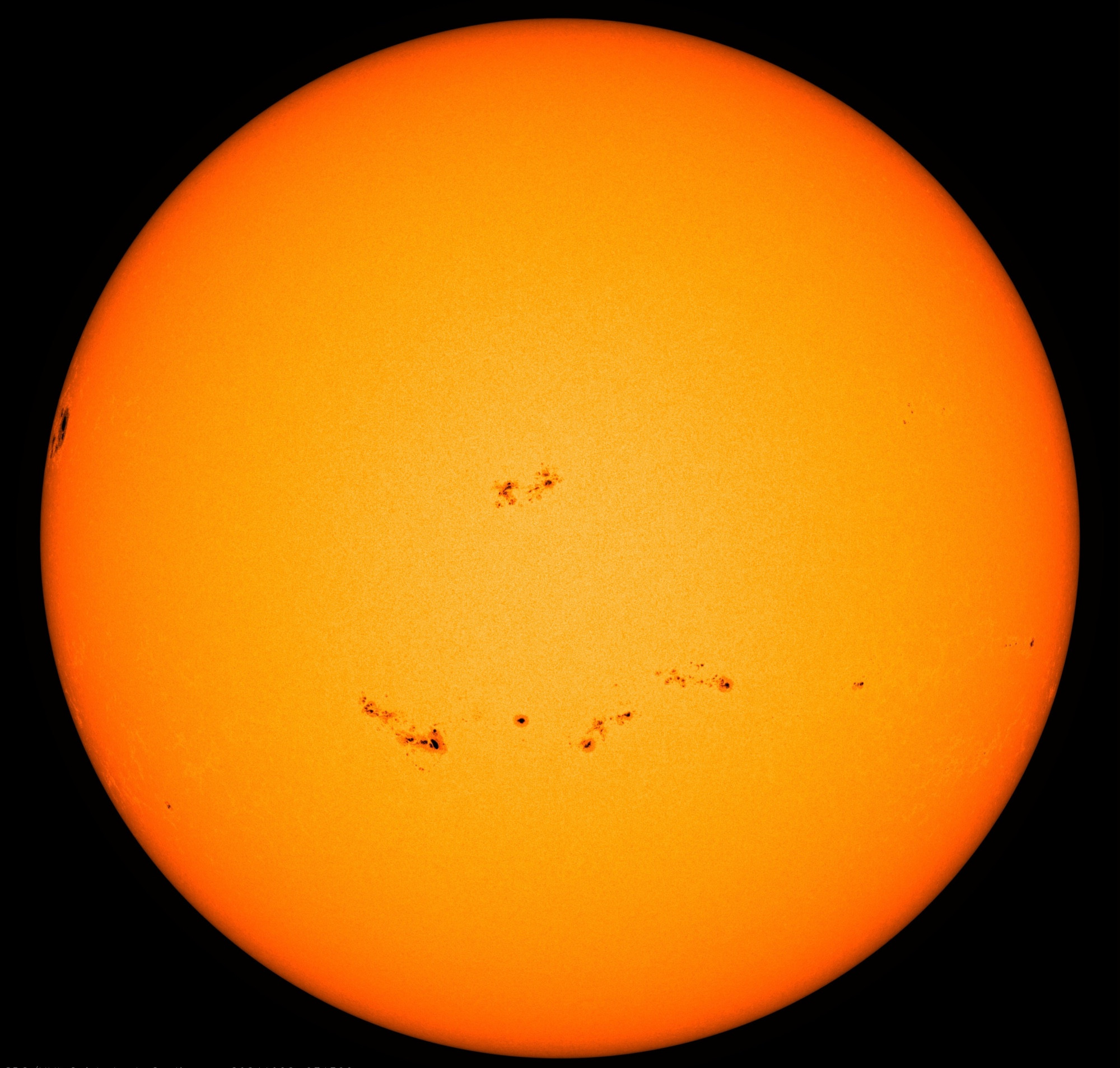 Die ganze erdzugewandte Seite der Sonne in gelber und leicht orangeroter Farbe. In dieser Darstellung ist die Oberfläche nahezu glatt. Die einzigen Strukturen werden von Sonnenflecken gebildet. Davon sind in beziehungsweise unterhalb der Mitte mehrere kleine als schwarze Punkte zu sehen. Ein deutlich größerer Sonnenfleck zeichnet sich ganz links am Rand ab.