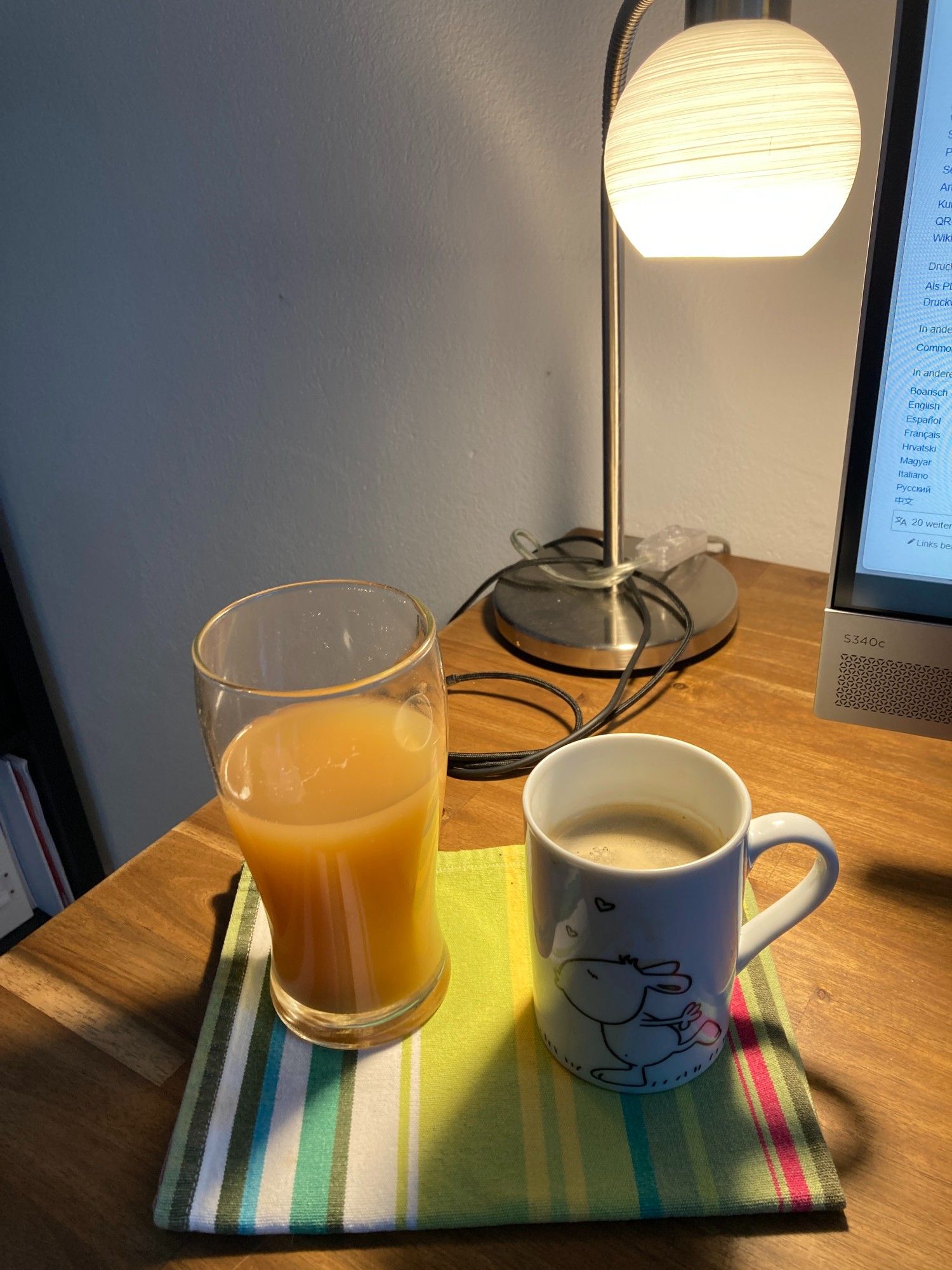 Großes Glas mit Apfelsaft g'spritzt und eine Tasse voller schwarzem Kaffee auf dem Schreibtisch stehend.