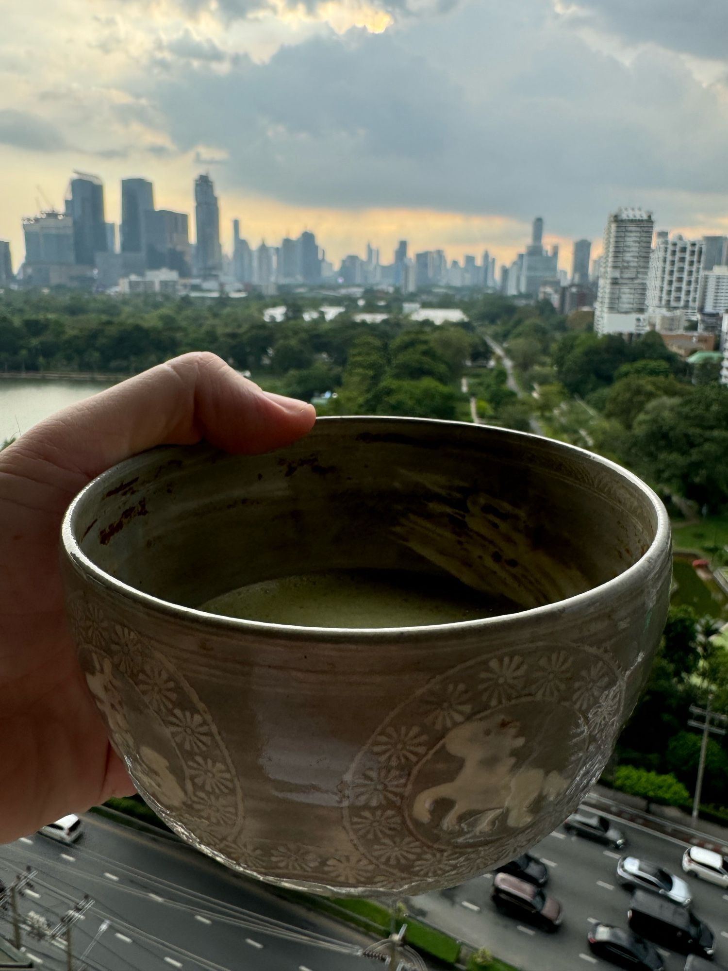 a grey matcha bowl with chinese zodiac characters around the outside held up on a balcony