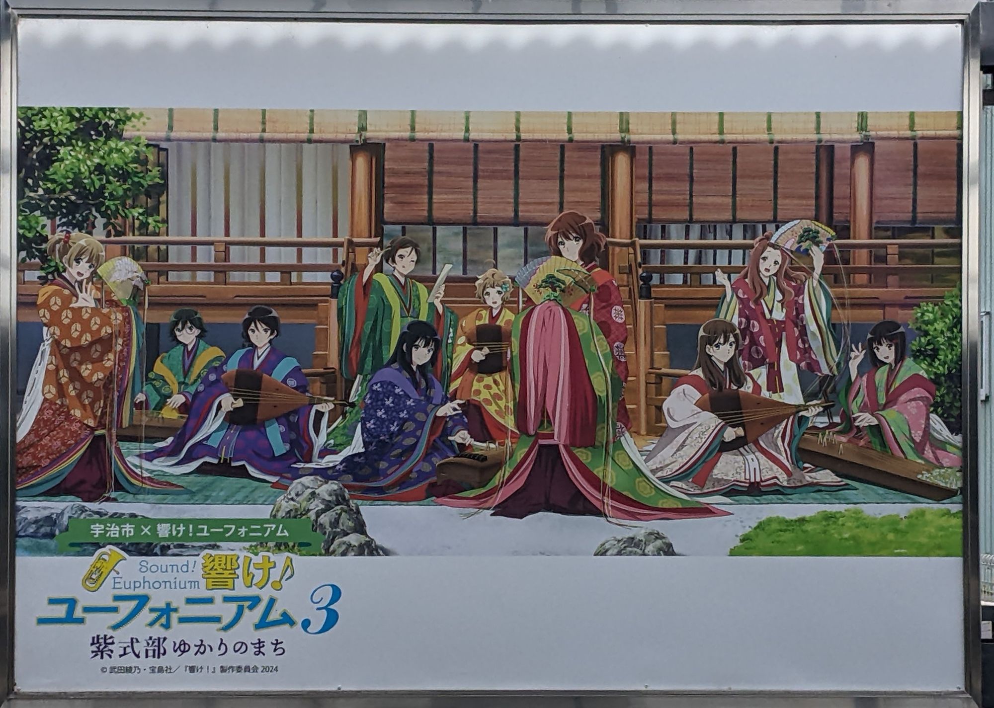 Une affiche avec une grande partie des personnages principaux d'Hibike Euphonium jouant des instruments traditionnels japonais devant une maison ancienne.