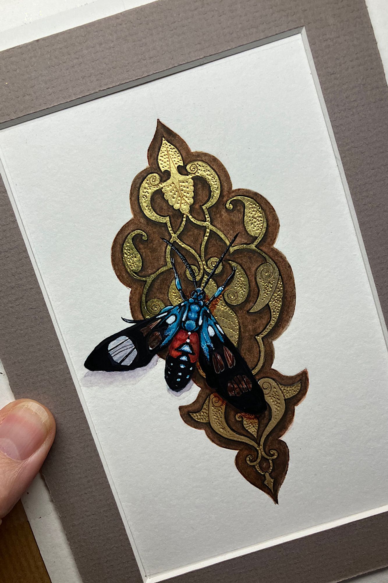 A colorful blue and red butterfly on a tooled gold leaf background