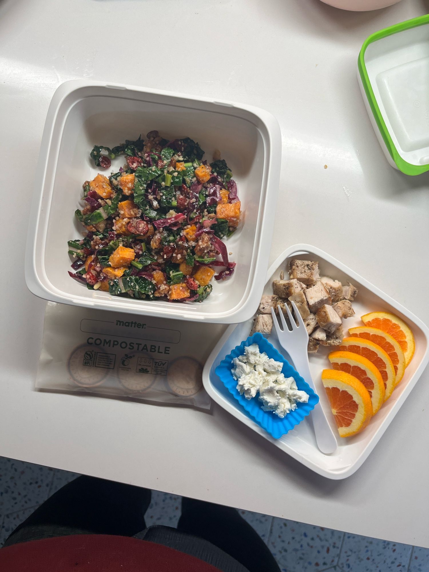 An OXO salad bento with a kale and sweet potato salad in the bottom, chicken, orange slices, and goat cheese, plus a compostable baggie of little cookies.