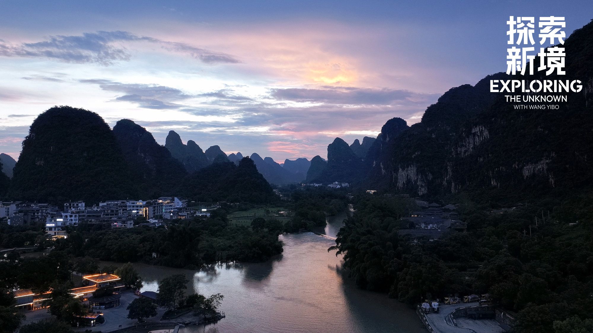 Night is falling over a river valley with strange, lumpy mountains, covered in greenery, seen from up high.