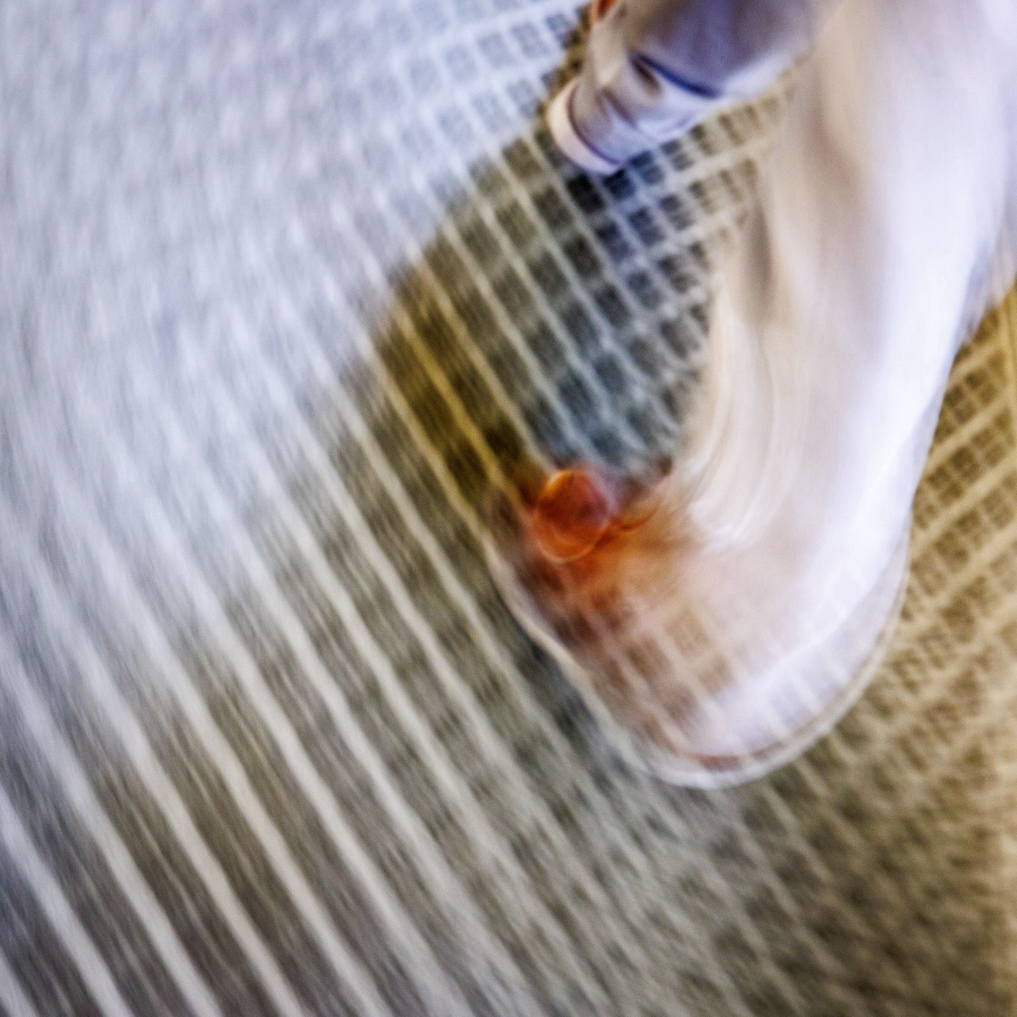 Color photo looking down at a carpet that has a grid pattern. There are also the lower legs and feet of someone walking in the upper right corner. A long shutter speed and the odd angle of view have resulted in a blurry image skewing all elements towards an abstract representation.