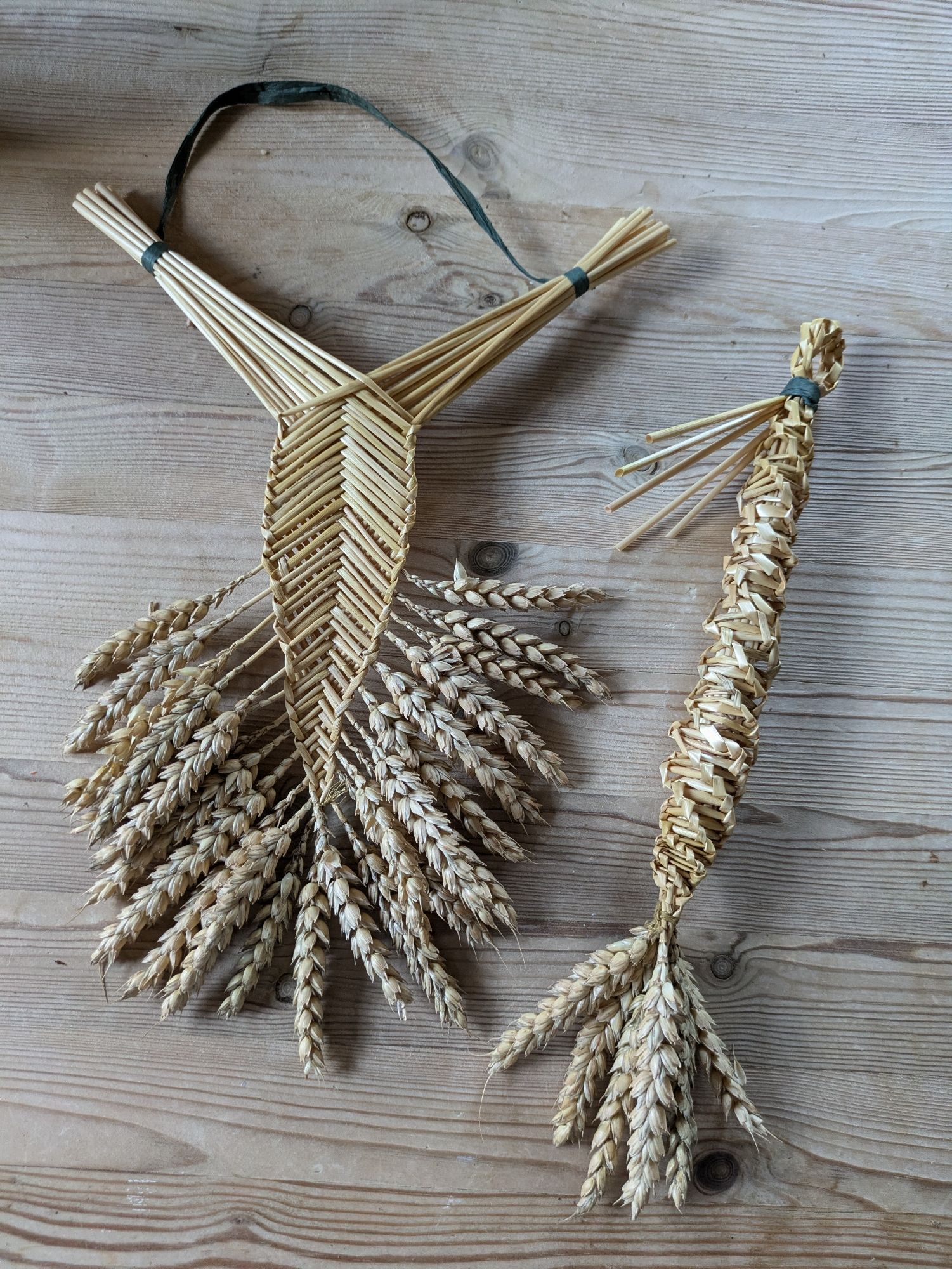 Two woven and plaited corn objects on wooden table