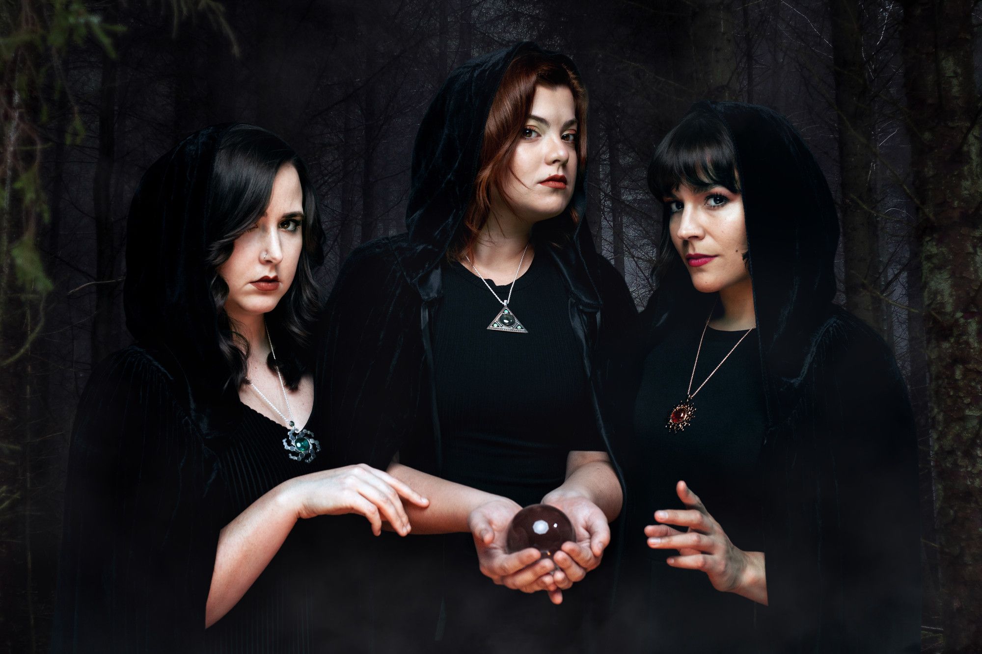 This is a promo shoot for the Amulet series, featuring three witches in the woods, each wearing a different amulet. They're in dark, hooded cloaks and are gathering around a crystal ball.