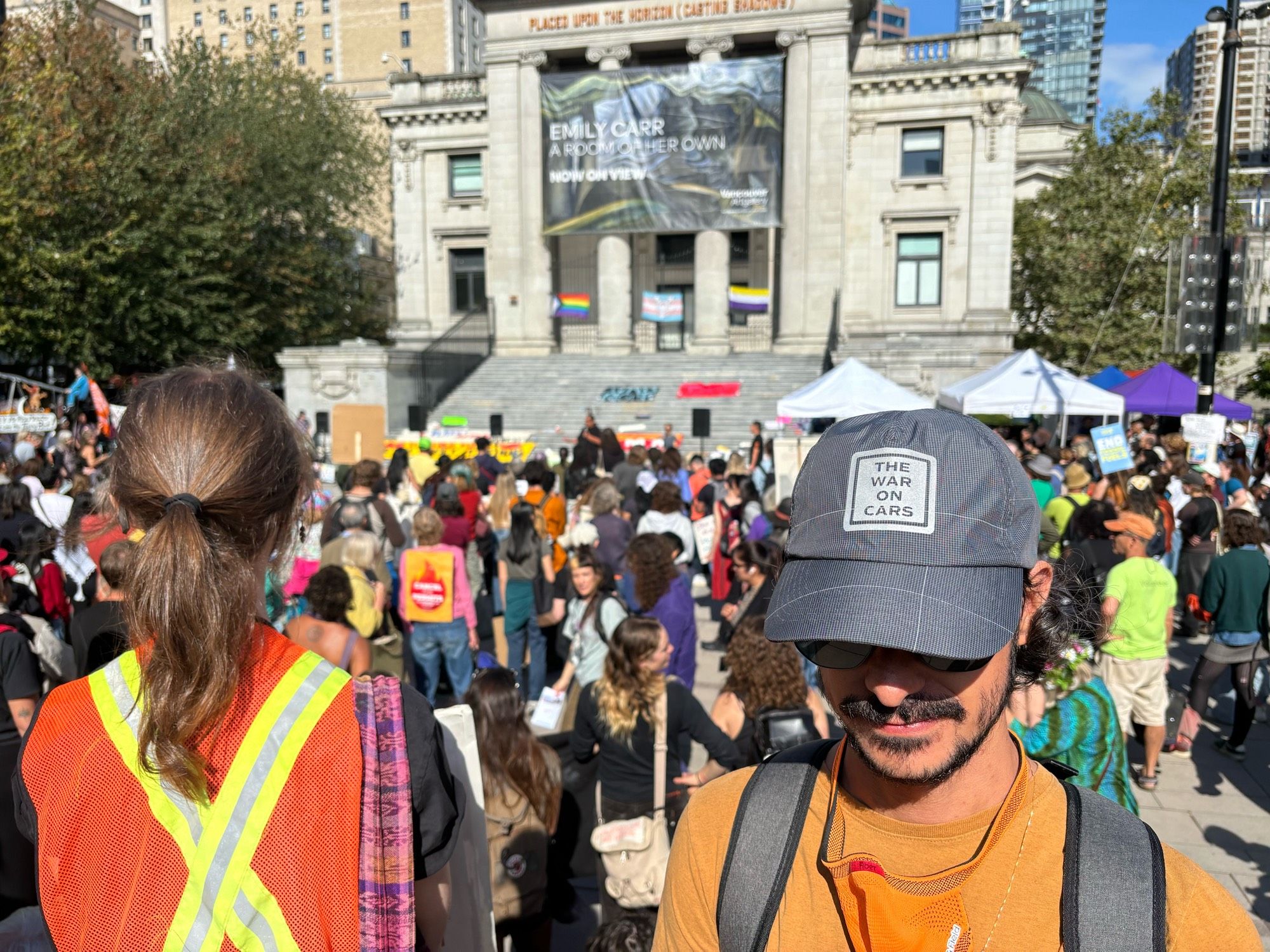 A protester in a “The War on Cars” hat stands in front of a protest crowd at the Vancouver Art Gallery.