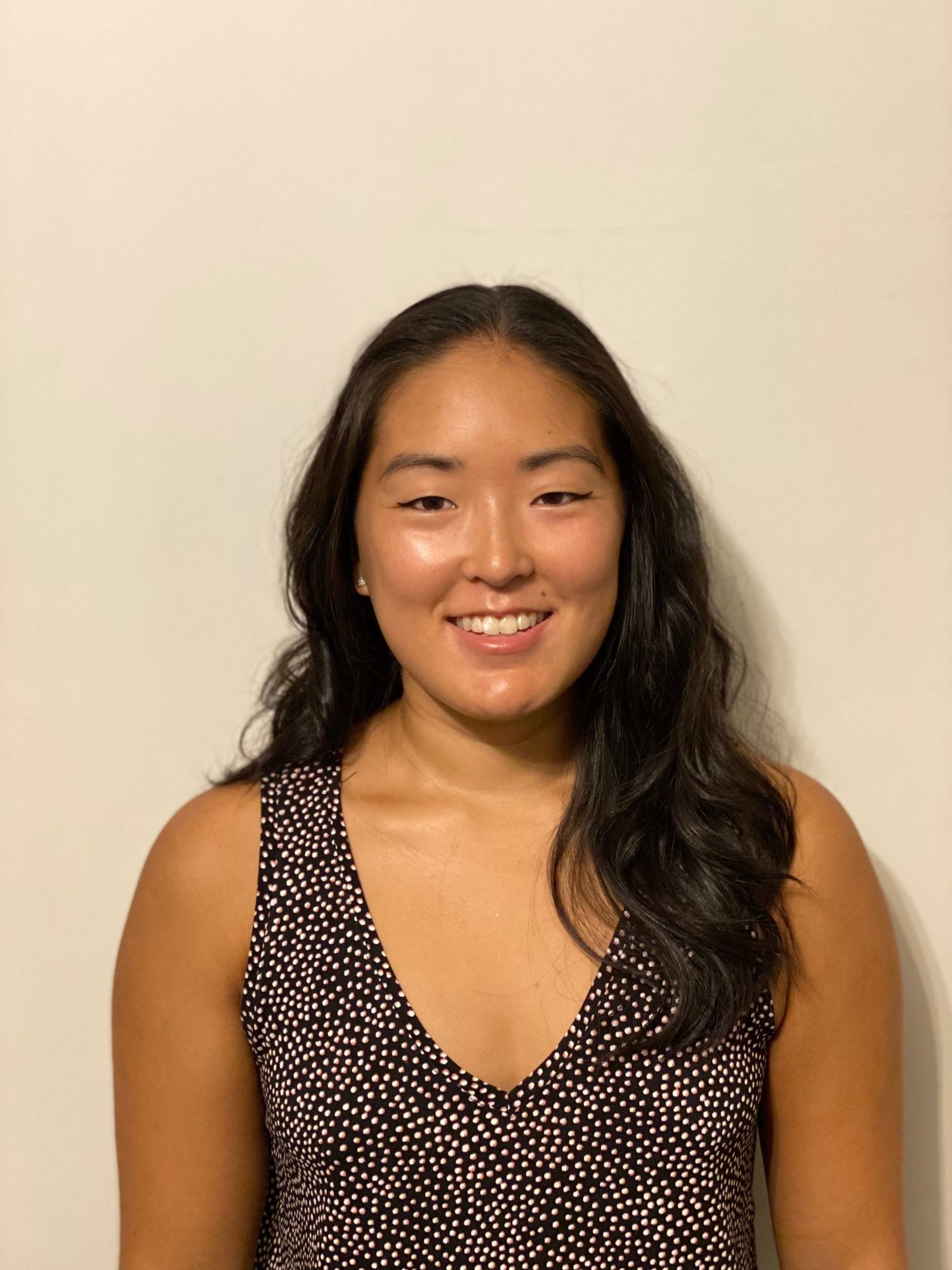 Headshot Asian woman with long black hair, wearing sleeveless black v-neck shirt with tiny white polkadots