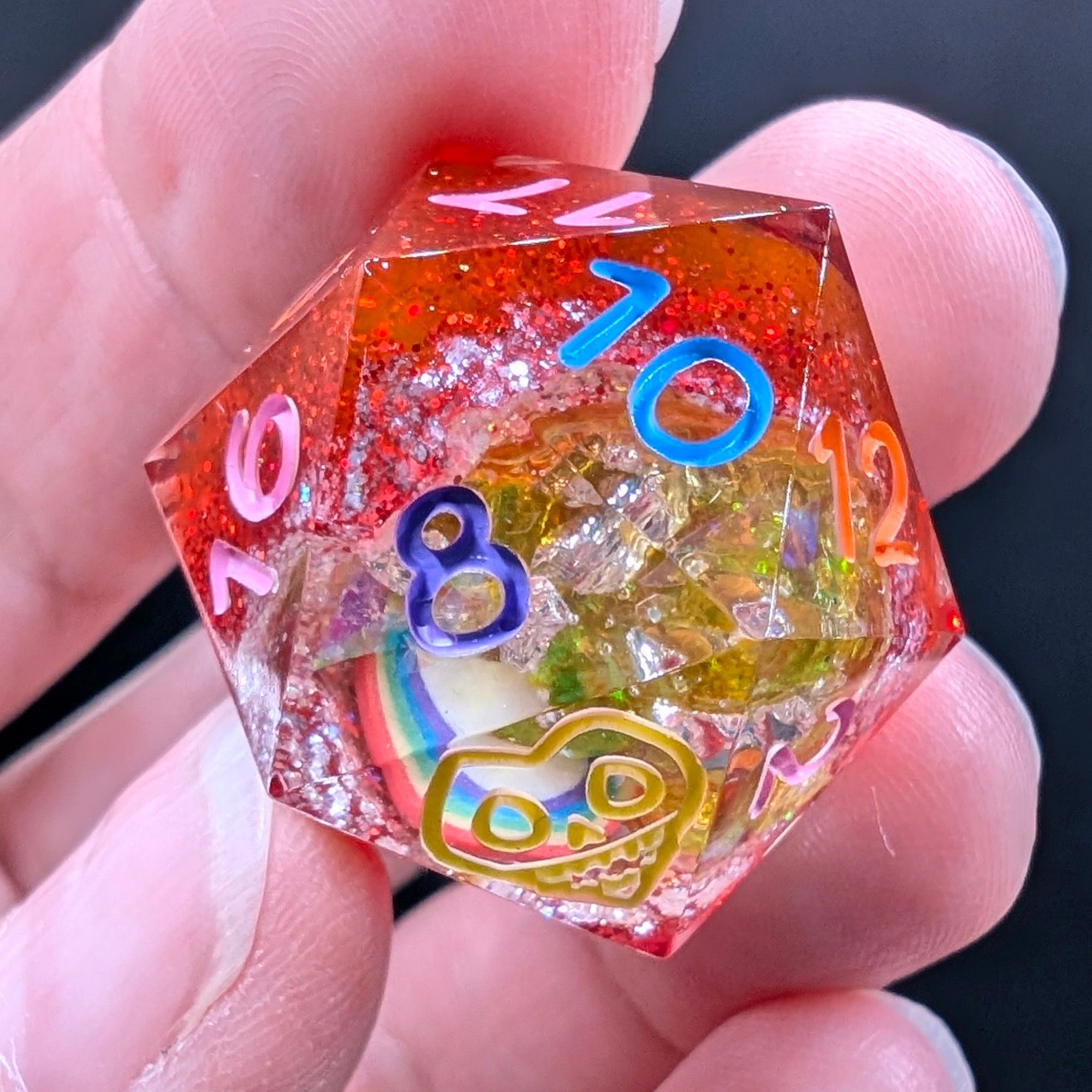 A close up of a d20 from a set of polyhedral dungeons and dragons dice. These are geode dice. The base is glittery ruby red, and the inside dung out part is painted a glittery white with yellow glitter flakes and a little rainbow inclusion.