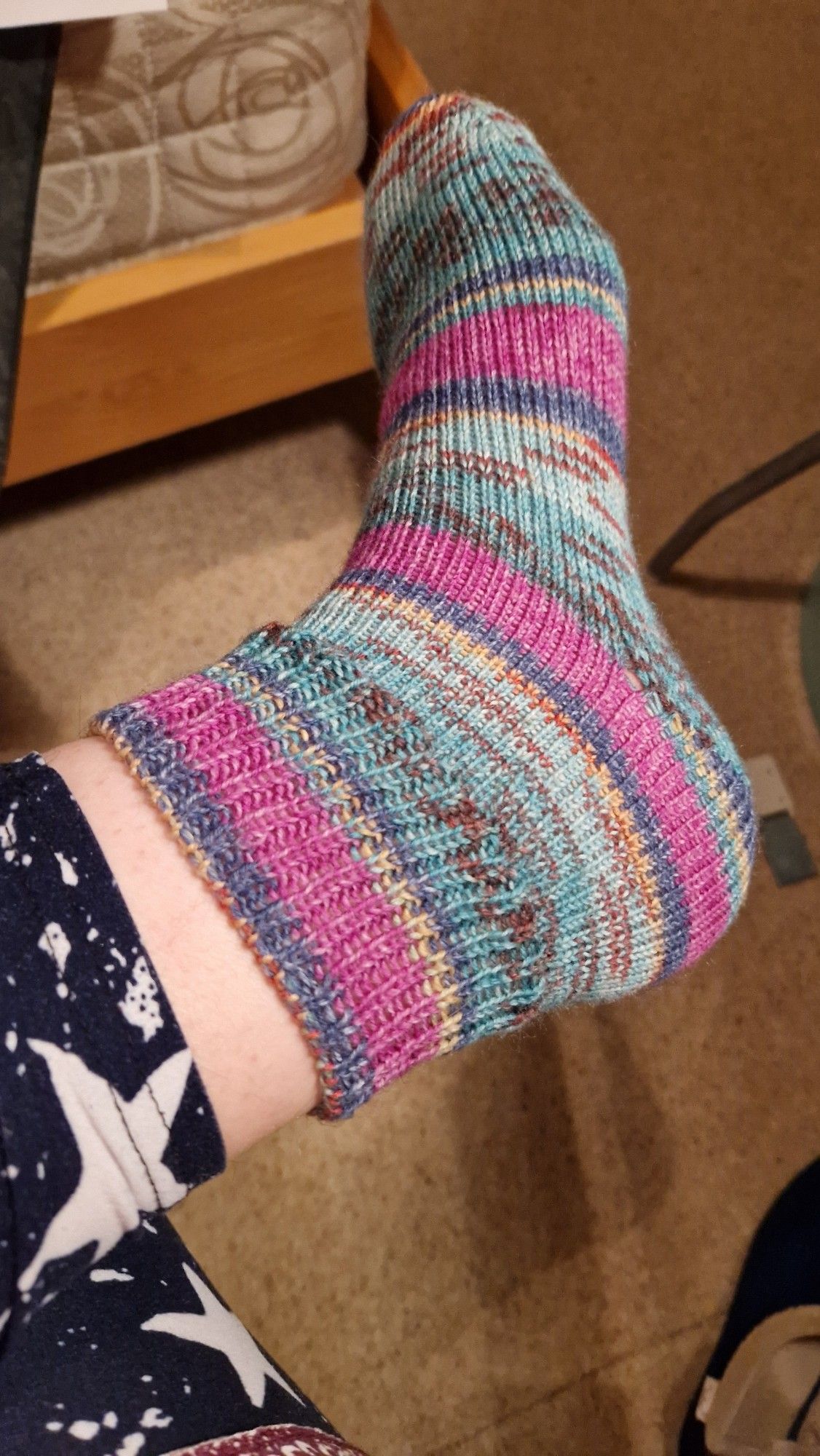 A left foot wearing a rather snazzy knitting sock in a mixture of blue, pink, yellow and brown.