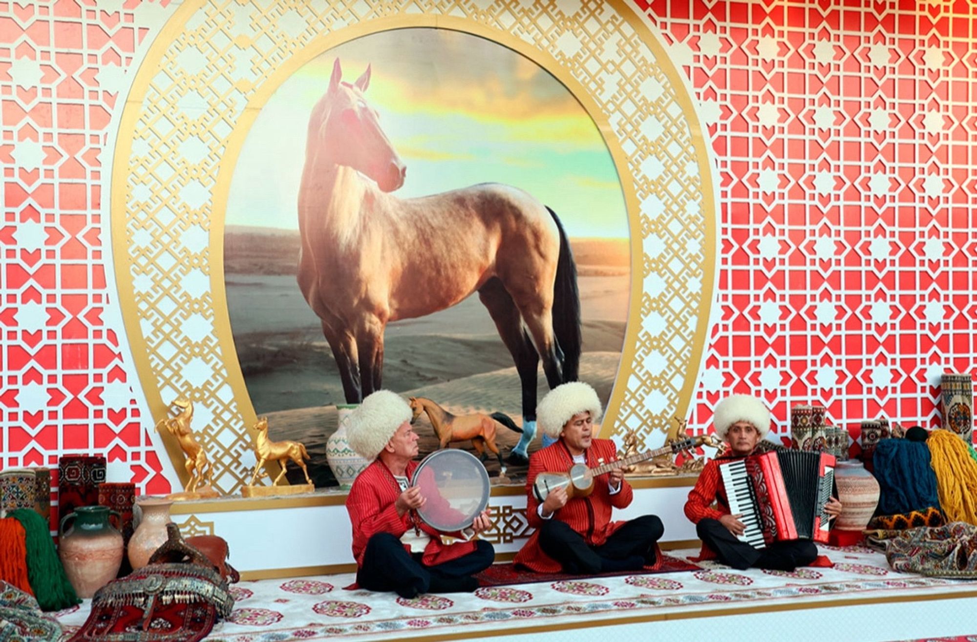 Turkmen musicians in front of a picture of a lovely horse. One has an accordion.