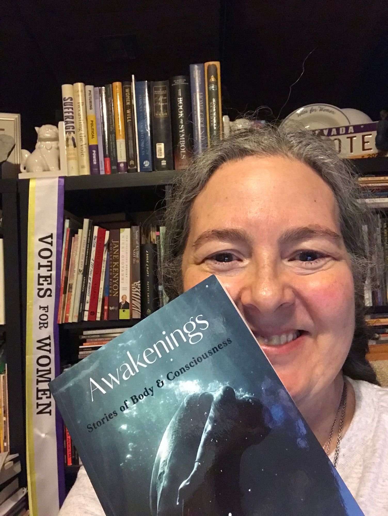 Happy contributor smiling with the book, Awakenings: Stories of Body & Consciousness