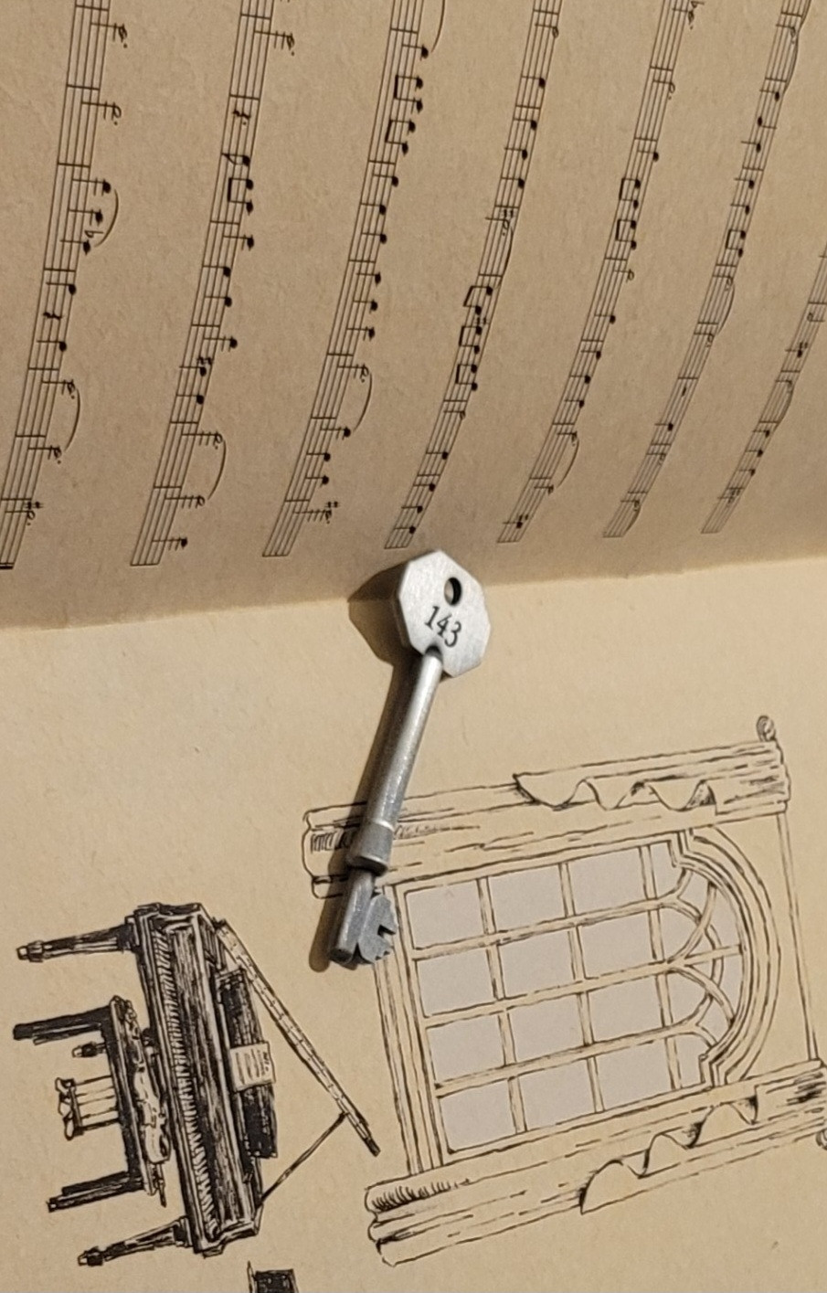 A key from the game Omori, a special item obtained the game, with the numbers 143 engraved on it, resting on sheet music for the song "Duet" that also features in the game.