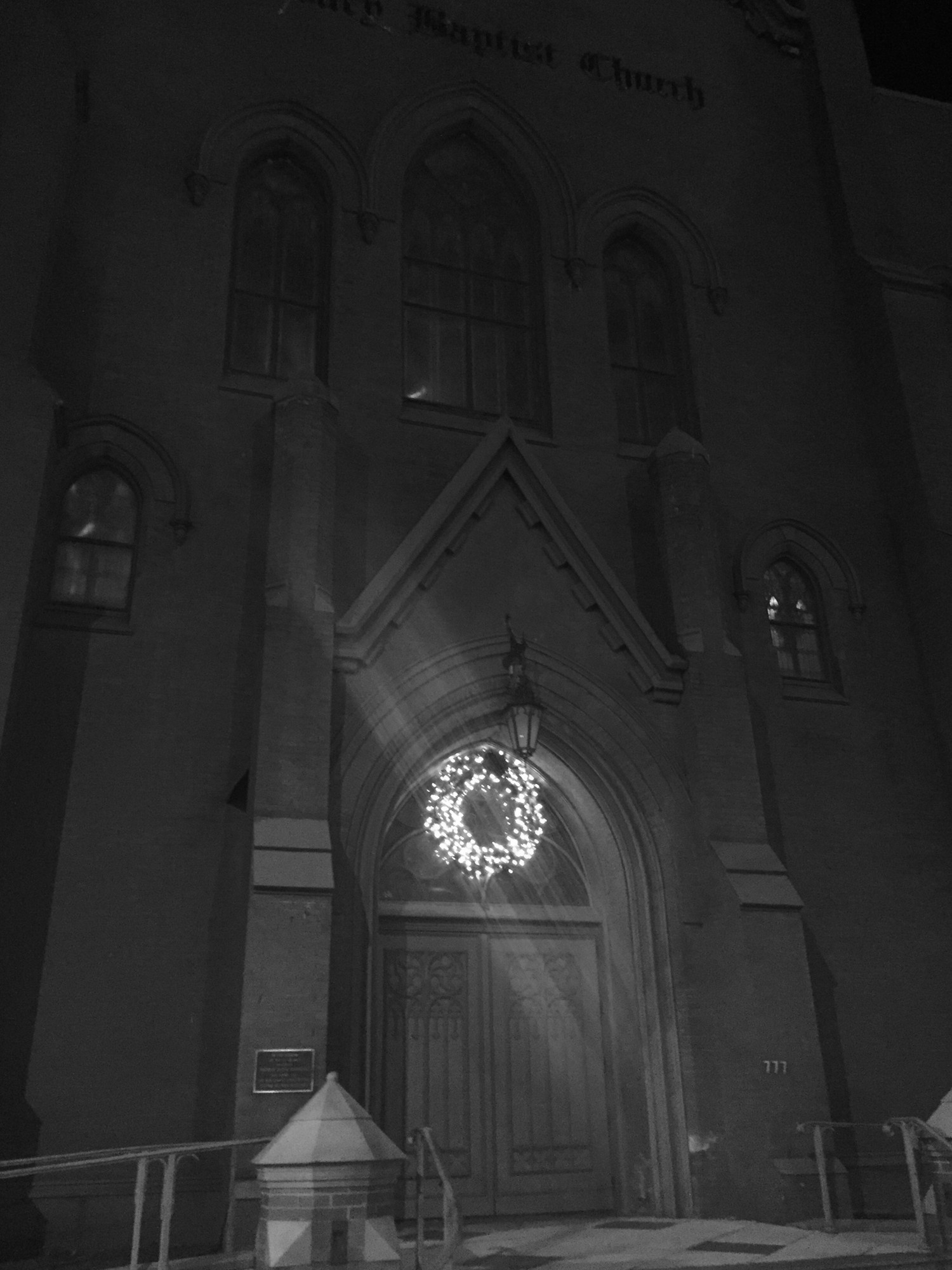 A lighted wreath on a church door in black and white.