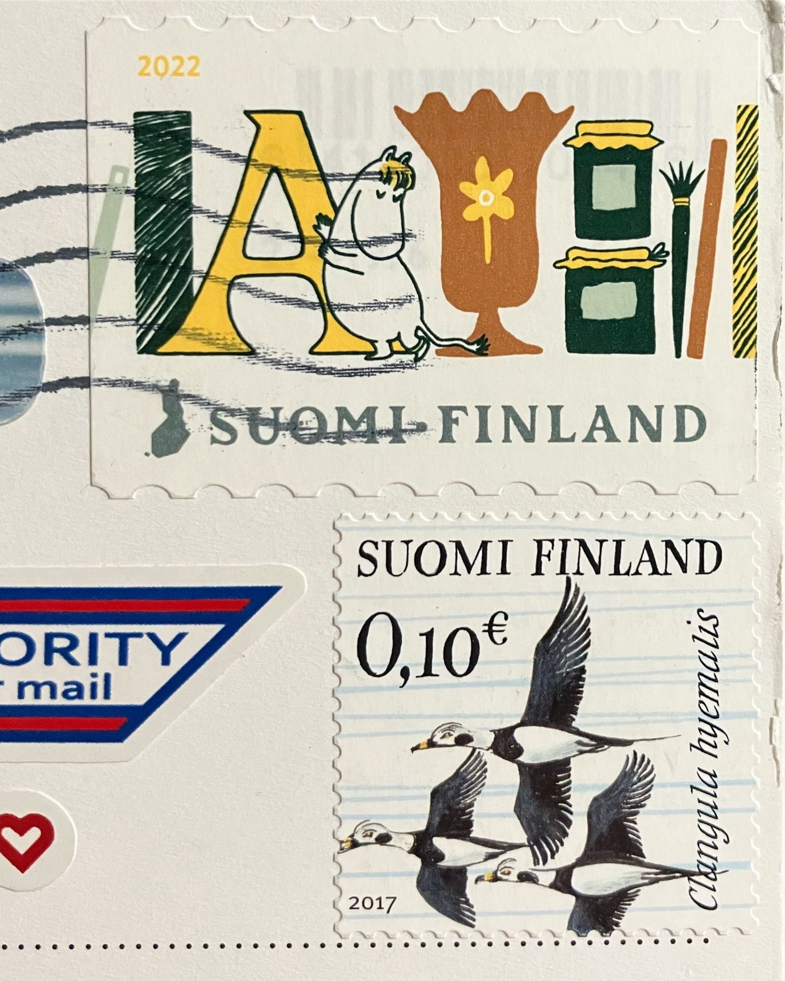 Two canceled Finnish stamps are shown. The top postage stamp shows Snorkmaiden leaning against a yellow letter A. The bottom postage stamp shows a trio of flying birds.