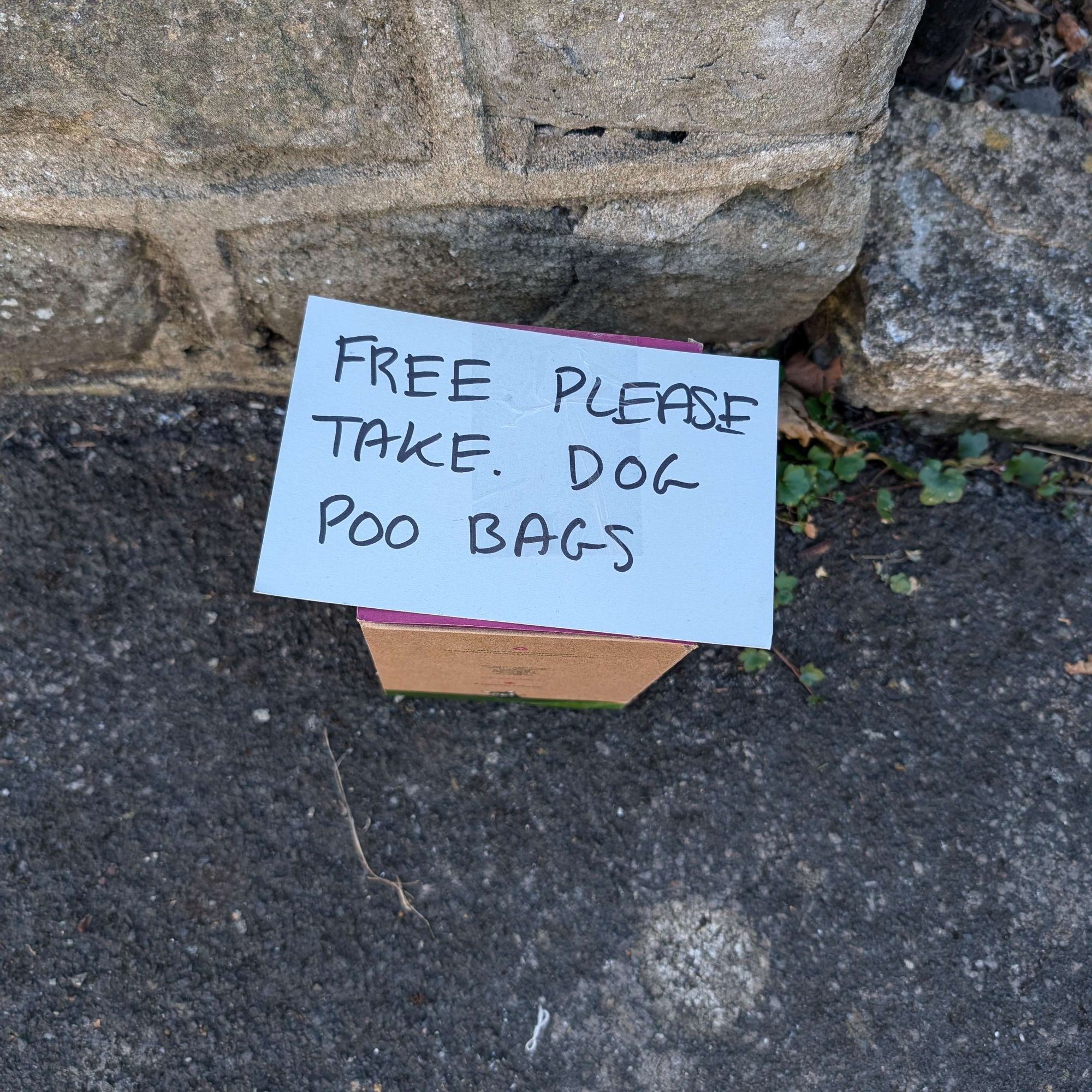 A small box left on a kerbside with a sign on top of it reading FREE PLEASE TAKE. DOG POO BAGS