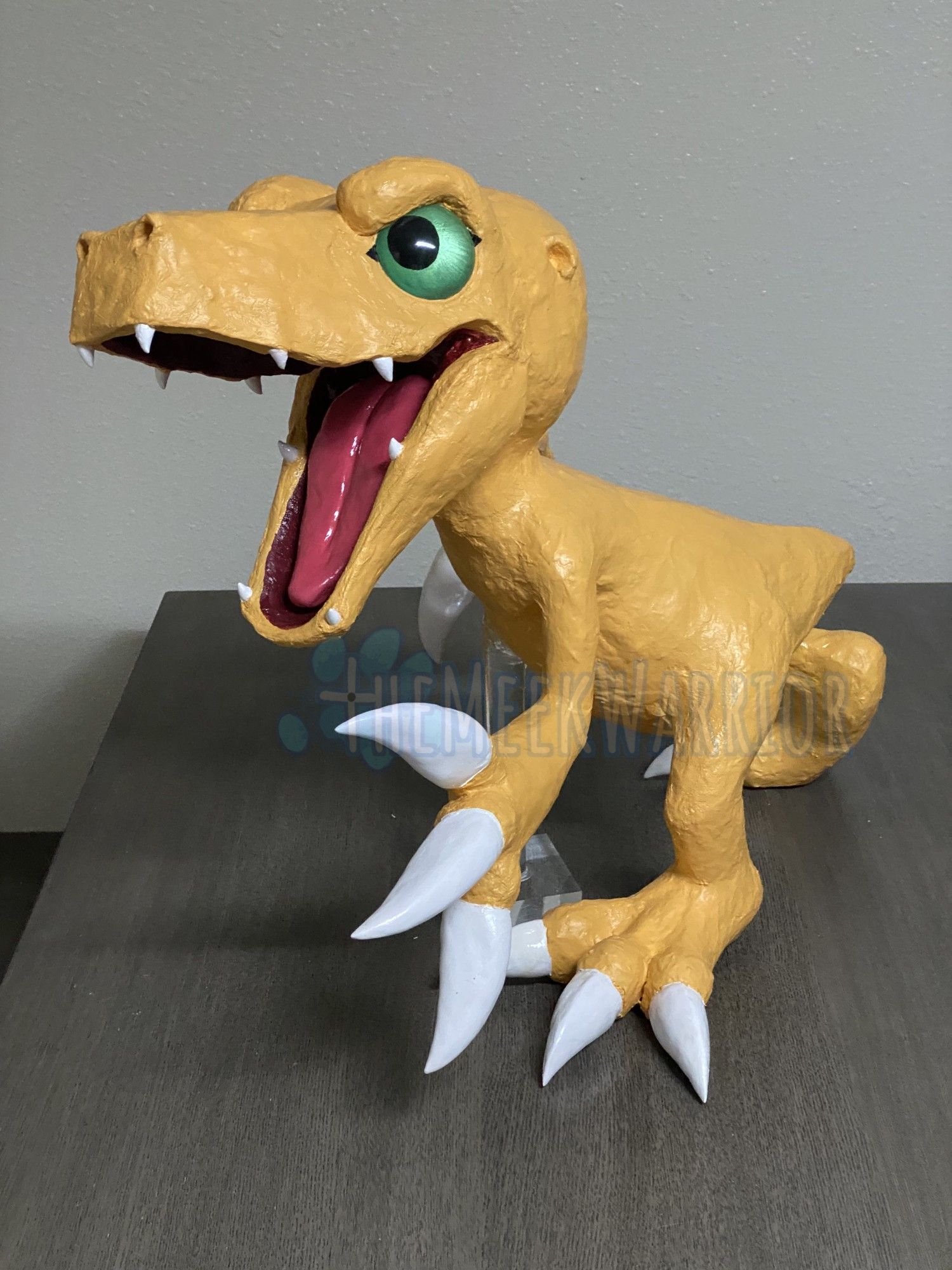 A paper mache sculpture of Agumon, an orange dinosaurian Digimon, lunging forward.