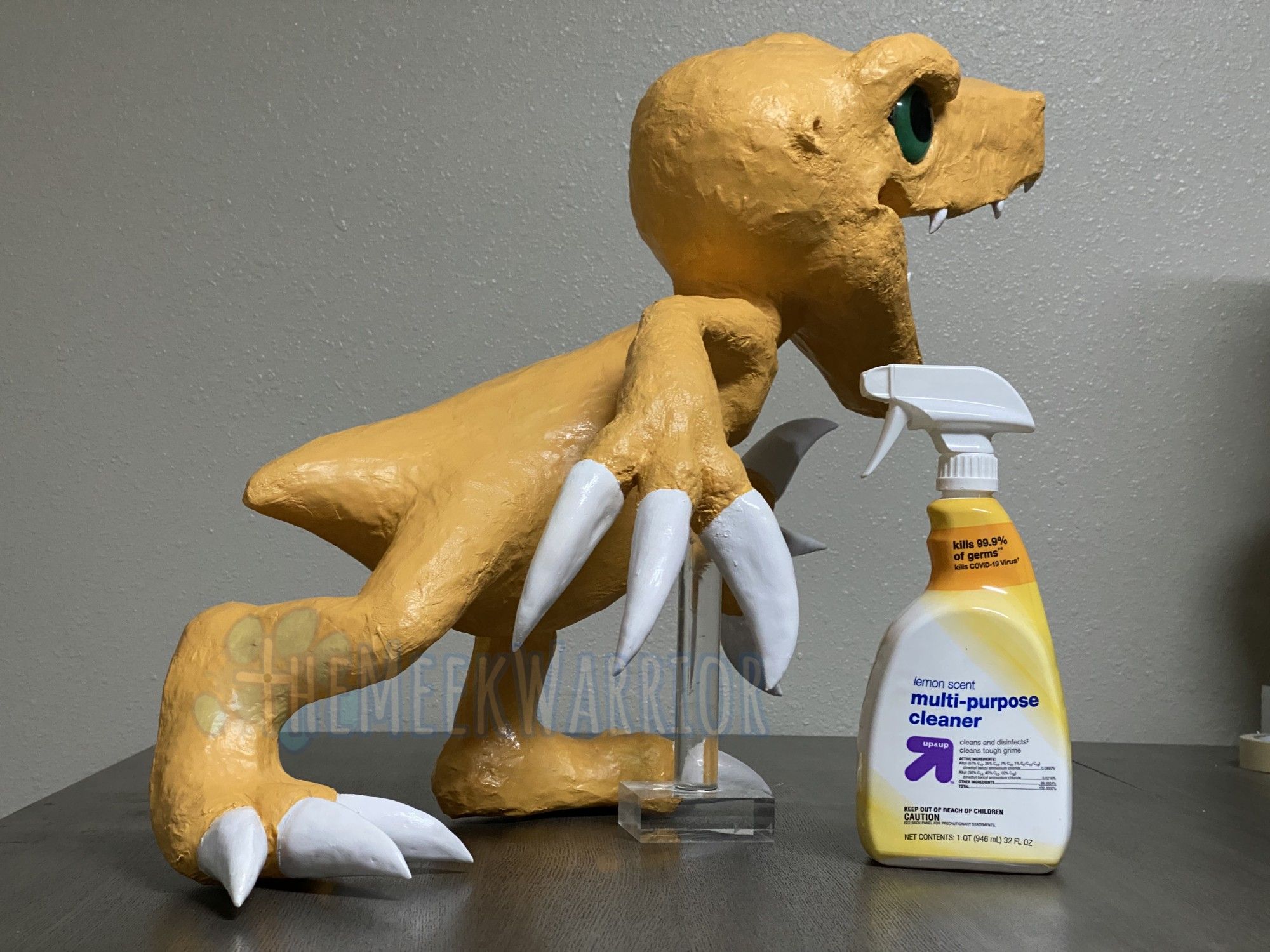 A size comparison of Agumon next to a bottle of cleaner, which reaches to his shoulder.