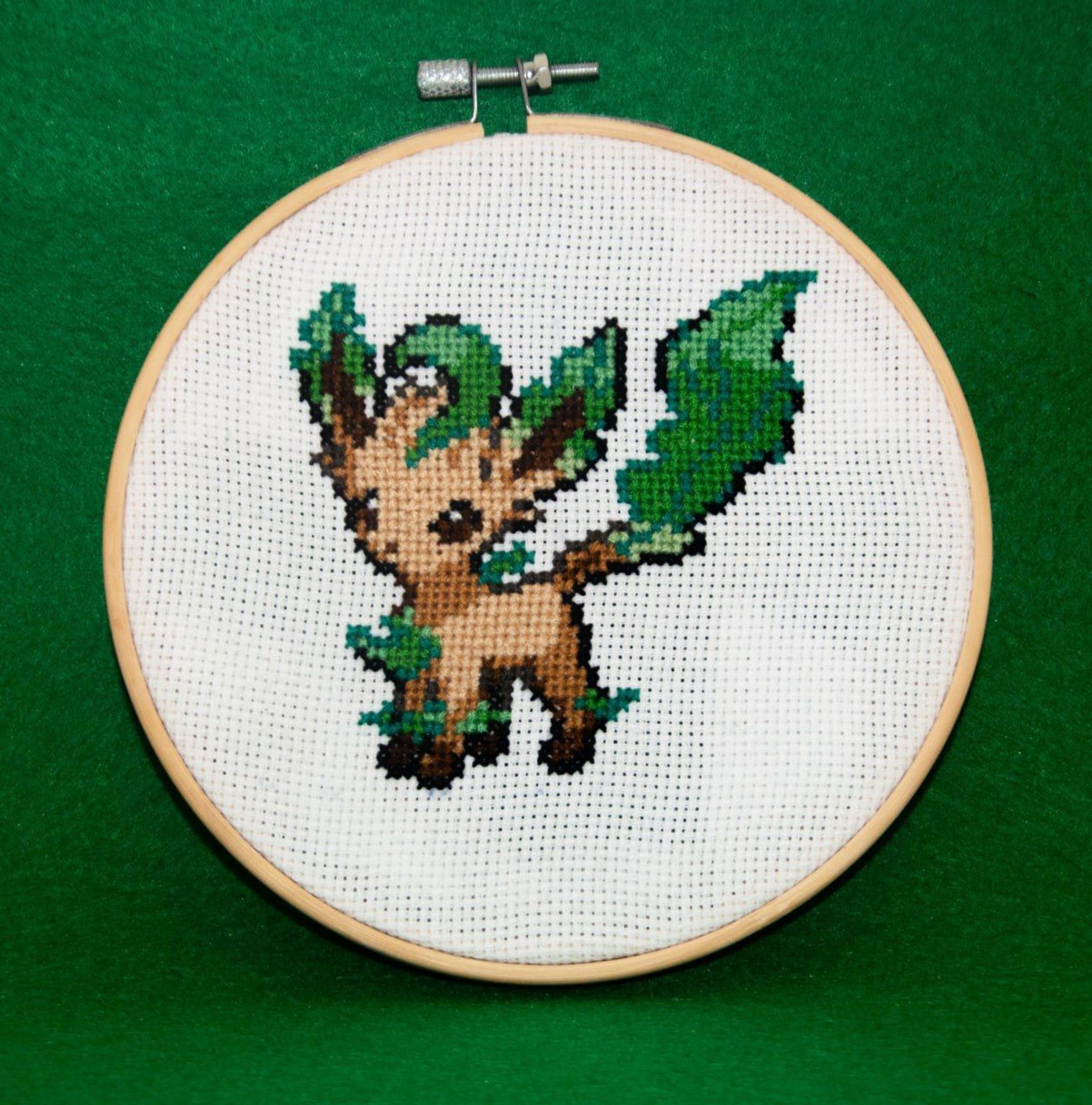 A cross-stich of a Leafeon Pokémon on a linen and wooden frame.