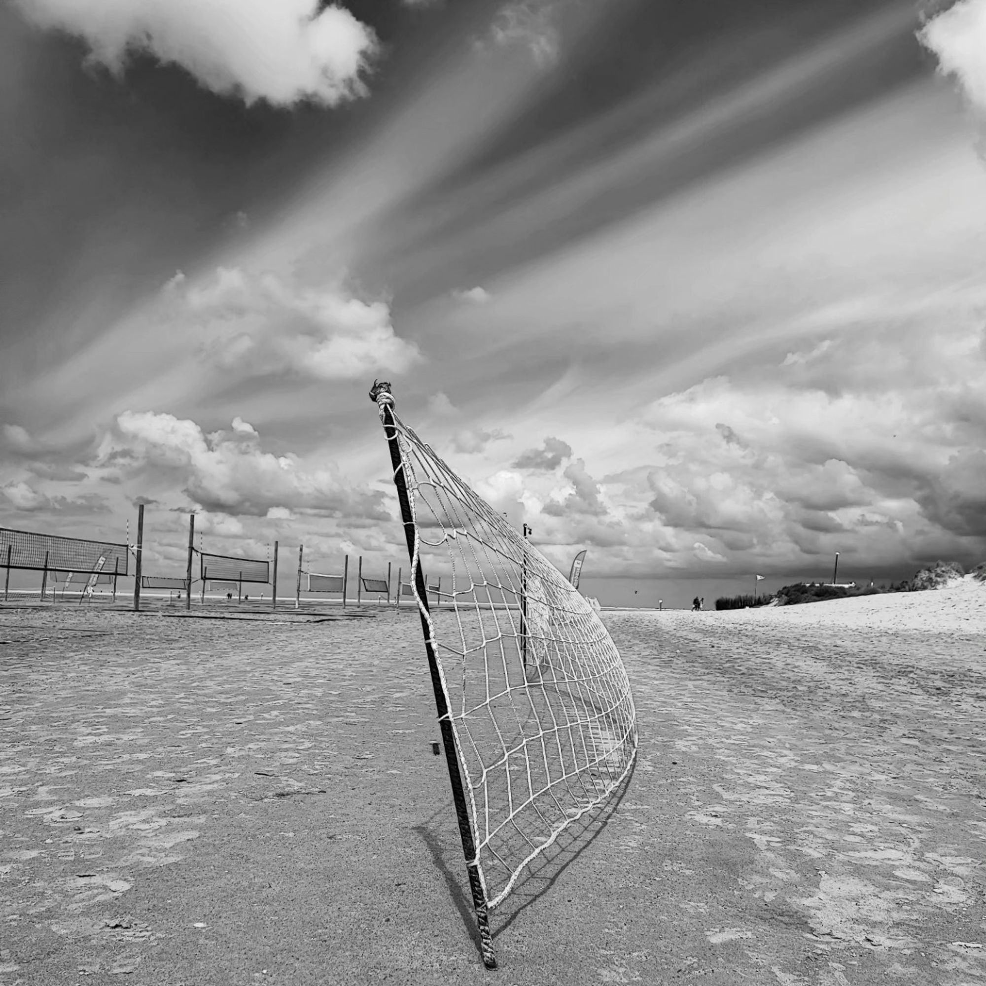 Ein Strandbild einfarbig grau.Verwischre Wolken und eine Reihe von Beachvolleyball Netzen nebeneinander vor einem leicht bewölkten aber einfarbig grauen Himmel .