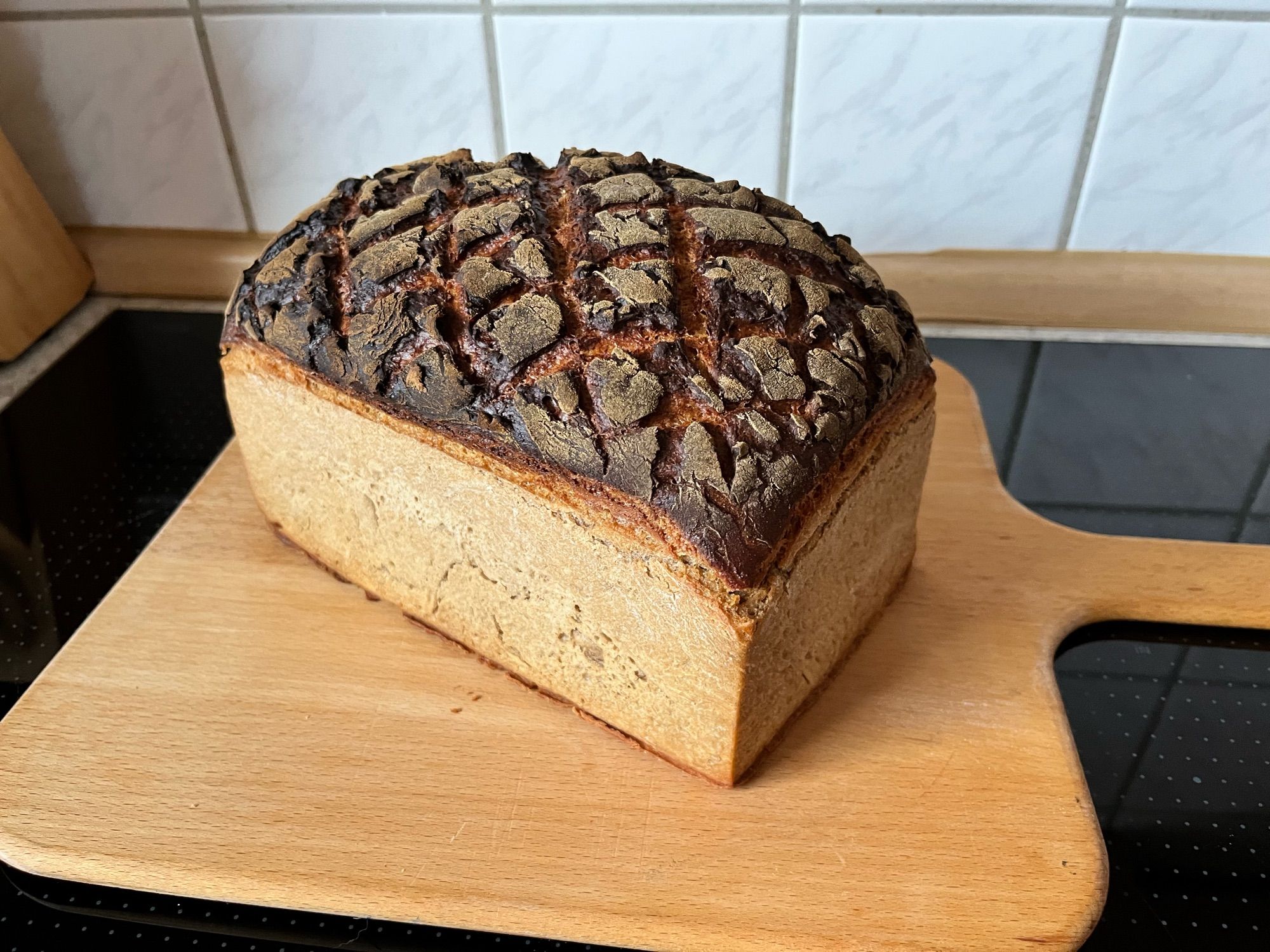 Auf einem Holzbrett liegt ein Kosakenbrot, kastenförmig, mit dunkler Kruste oben, die rautenförmig eingeschnitten ist.