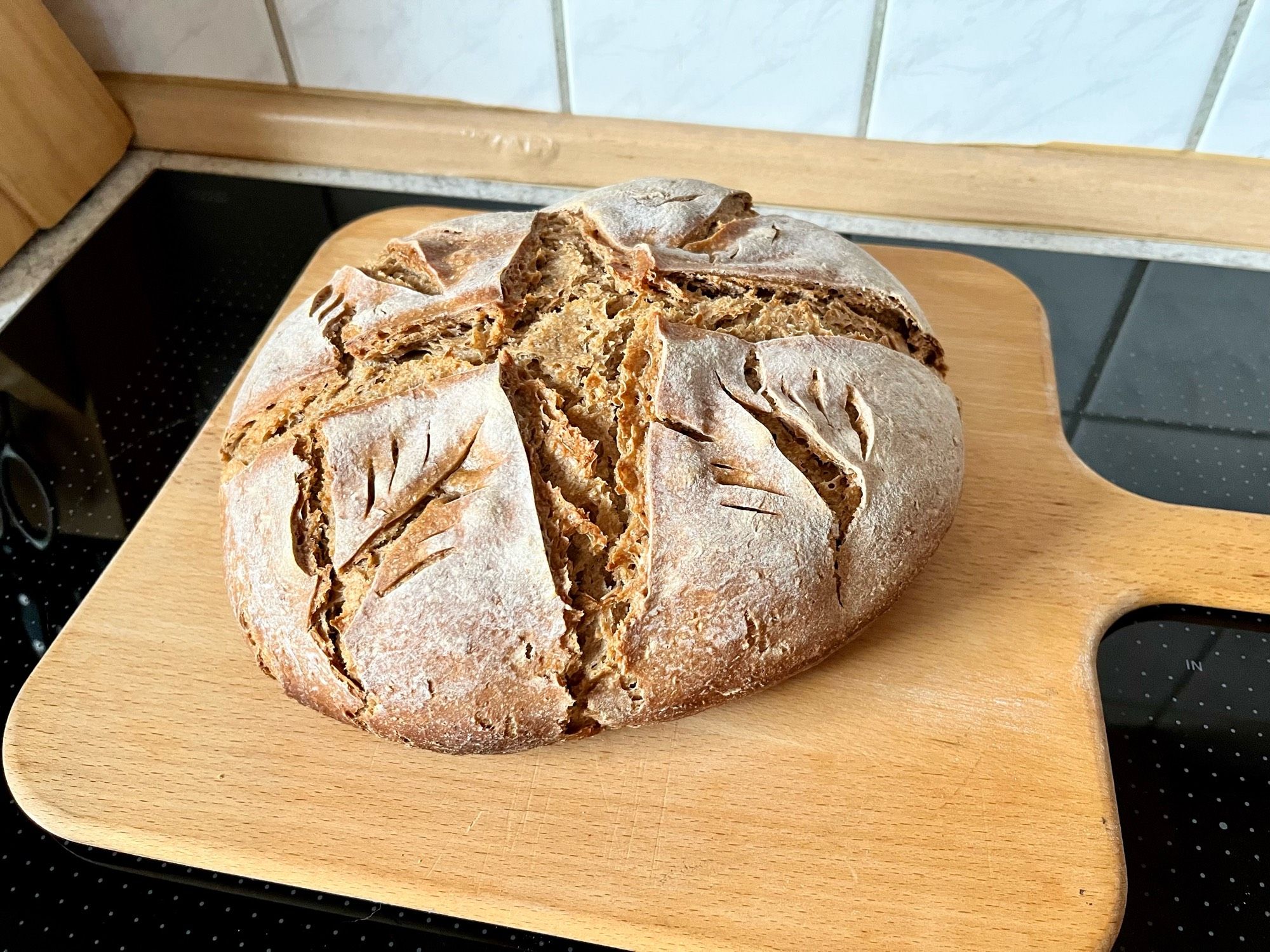 Auf einem Holzbrett liegt ein rundes Brot, die Kruste ist kreuzförmig eingeschnitten.