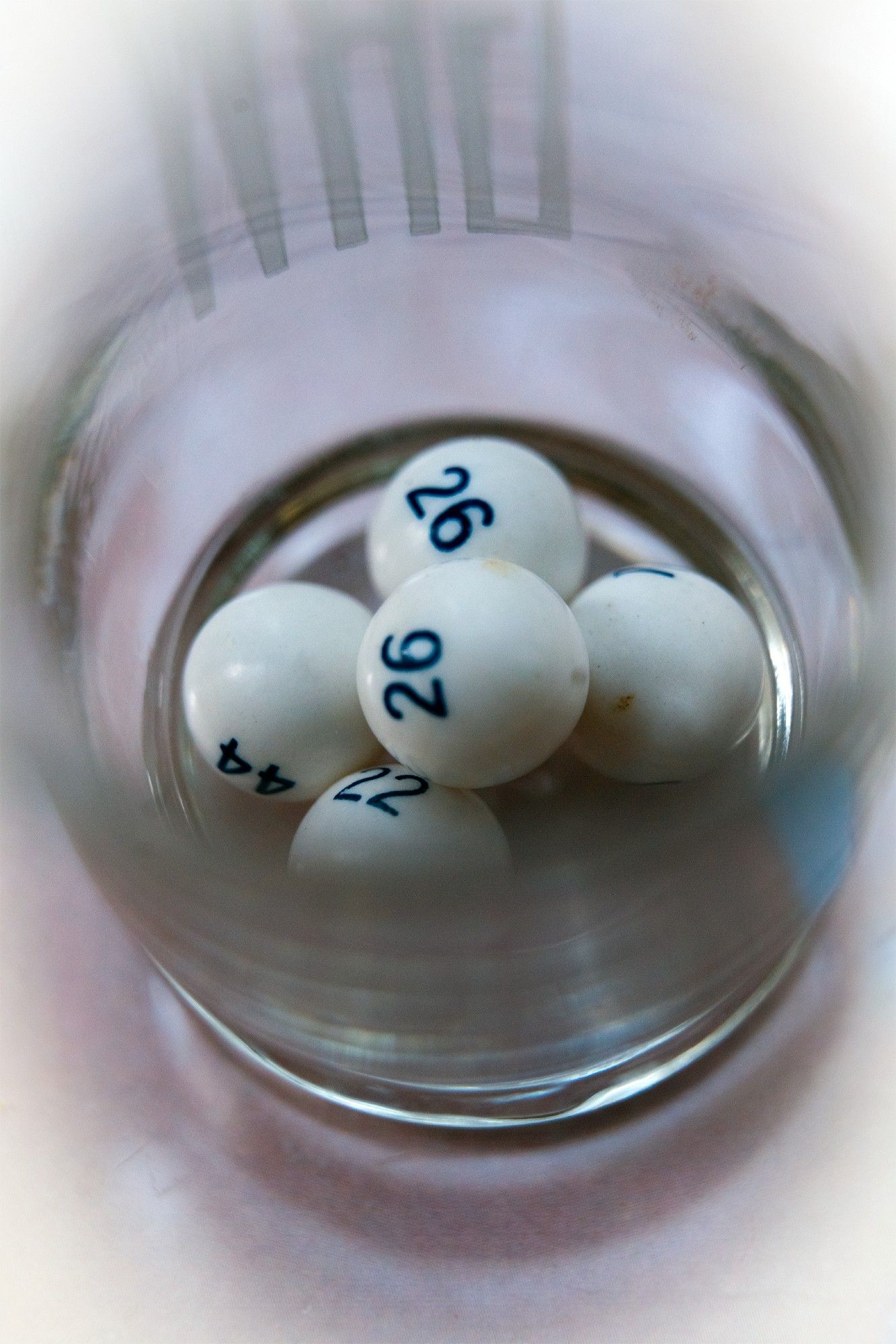 photograph of a glass with an etched monogram holding 5 white balls with dark blue numbers printed on them.