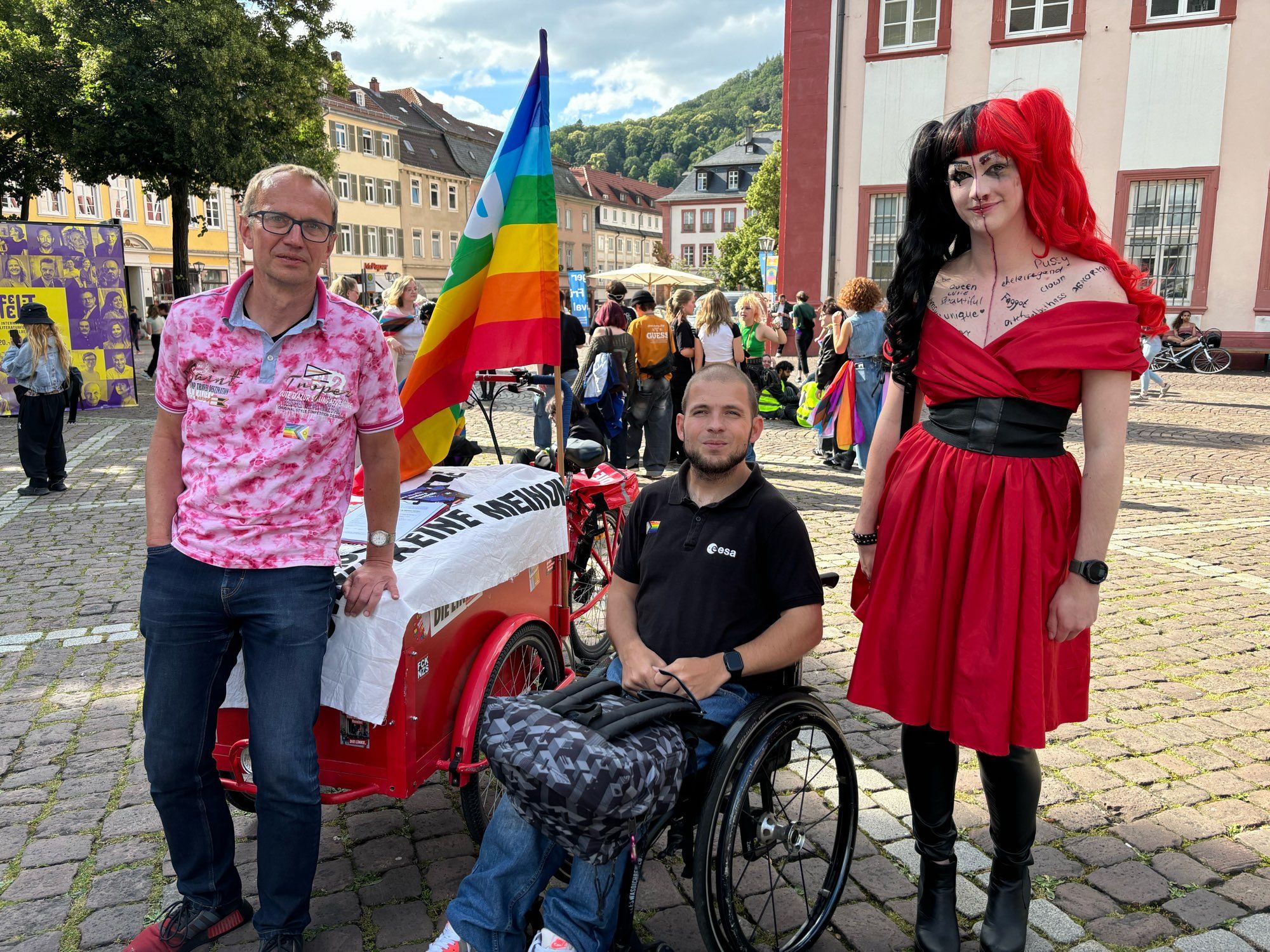 Die Linke Lastenrad mit pride Flag, einem Fußgänger, einem Rollifahrer und einer Drag Queen