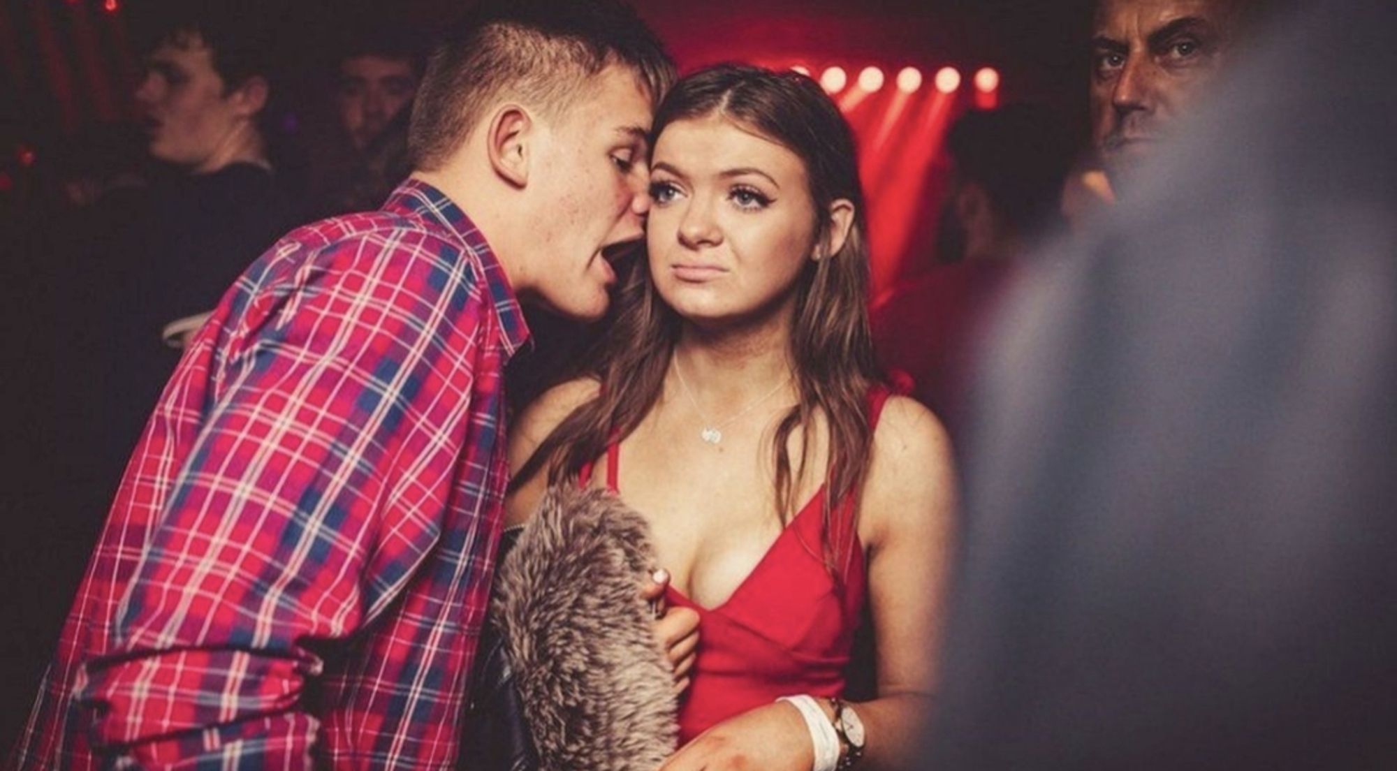 A guy talking loudly into the ear of an unimpressed girl at a club