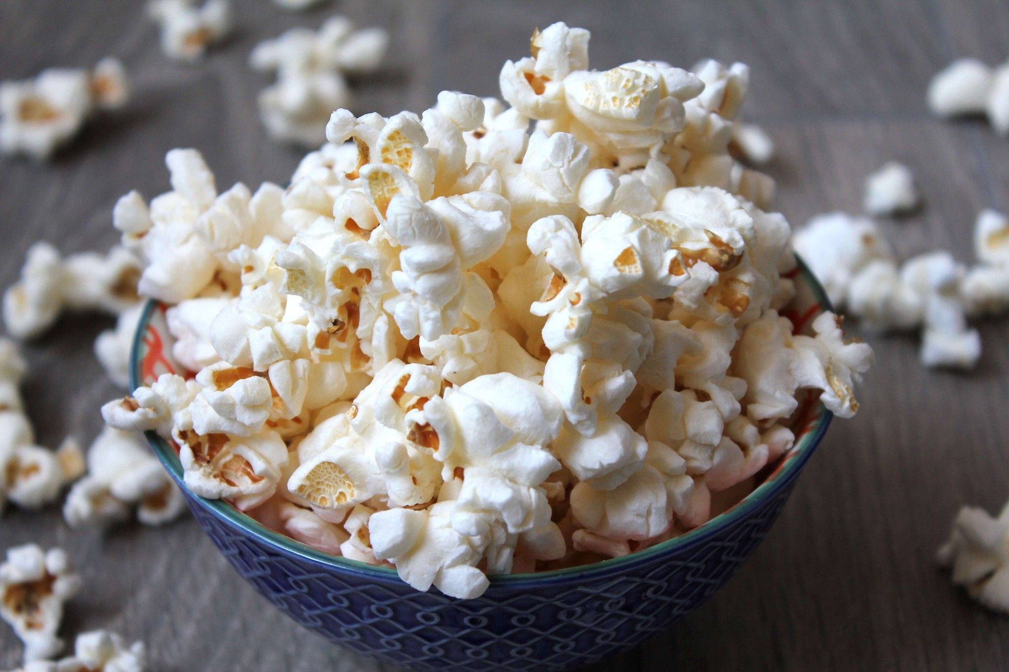 A small blue ceramic bowl filled to overflowing with light fluffy popcorn