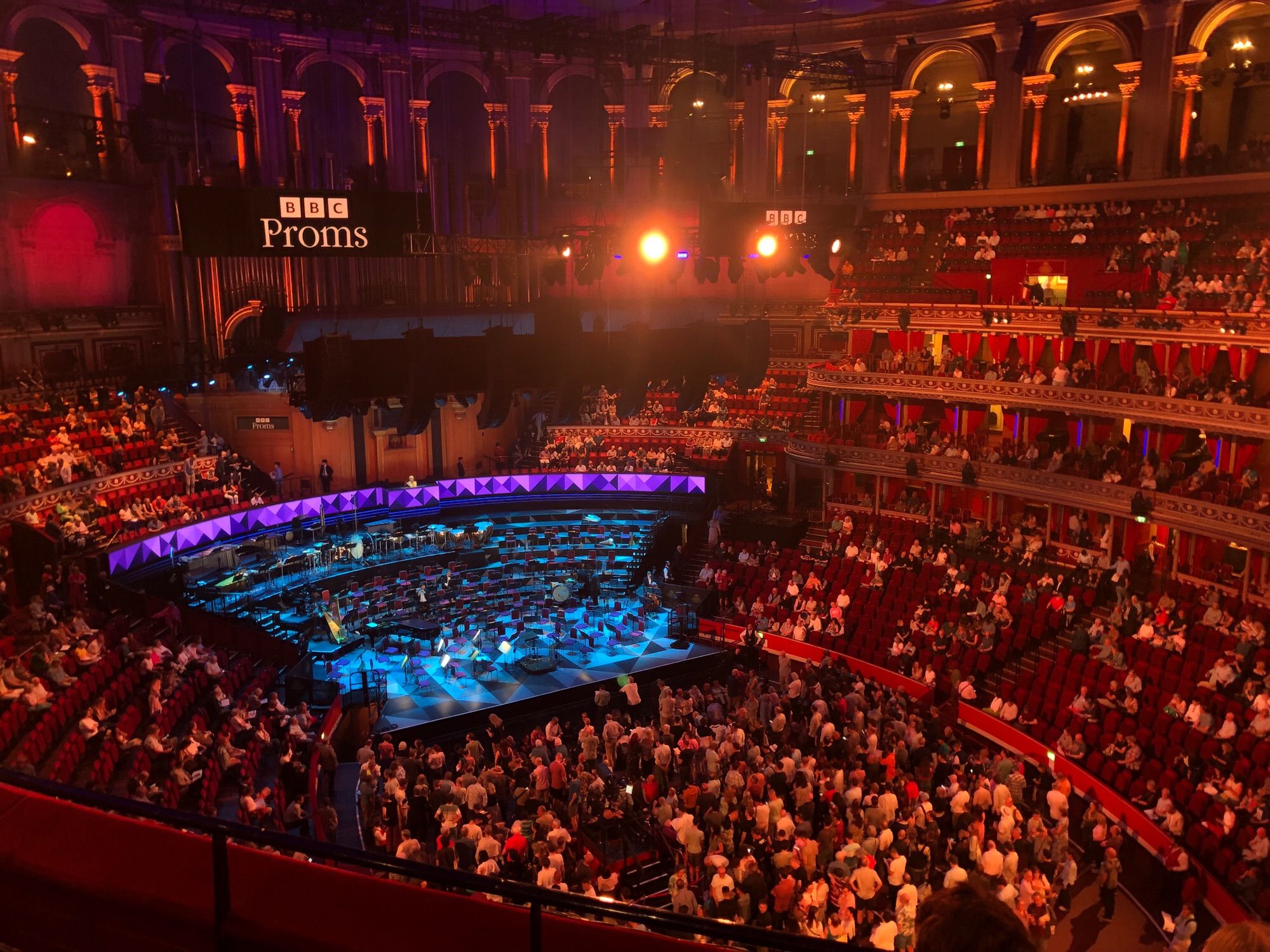 Inside of the Royal Albert Hall the stage is empty bathed in blue the seats are starting to fill