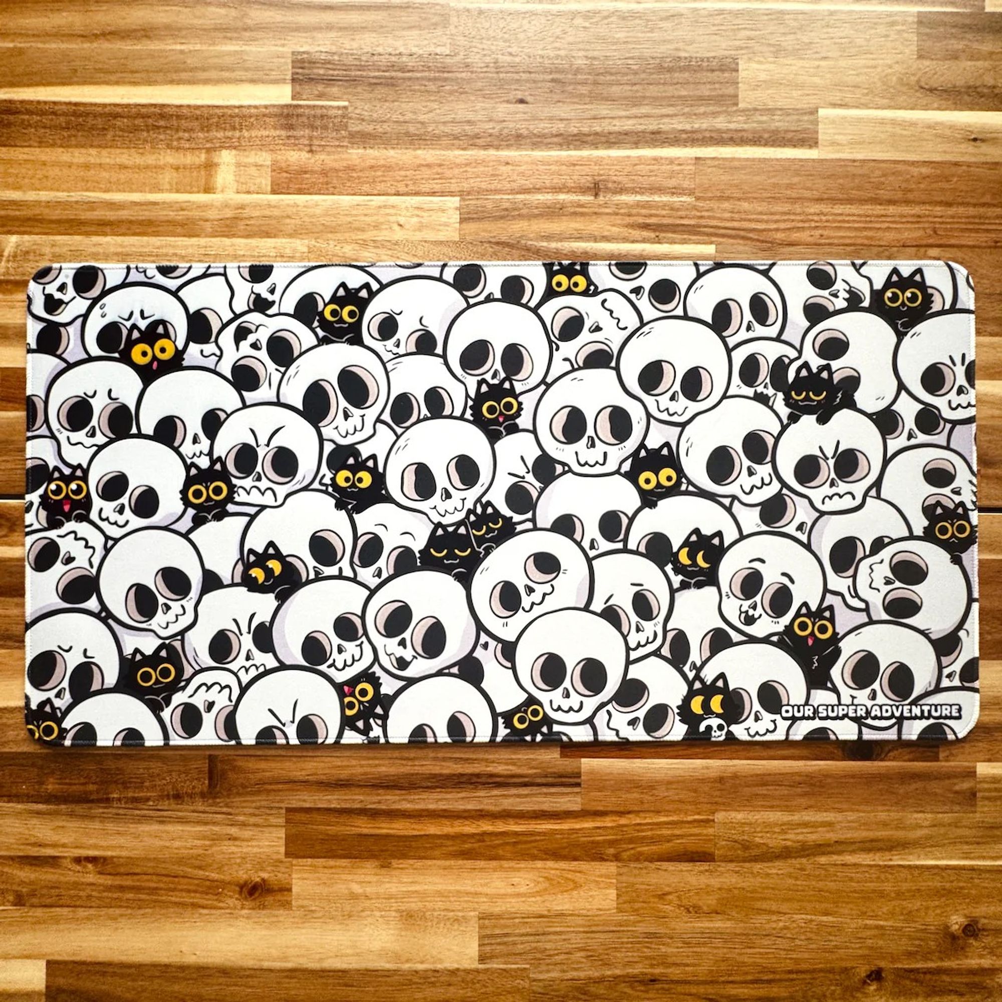 A photo of a large gaming mouse pad, featuring skulls and lots of tiny black cats.