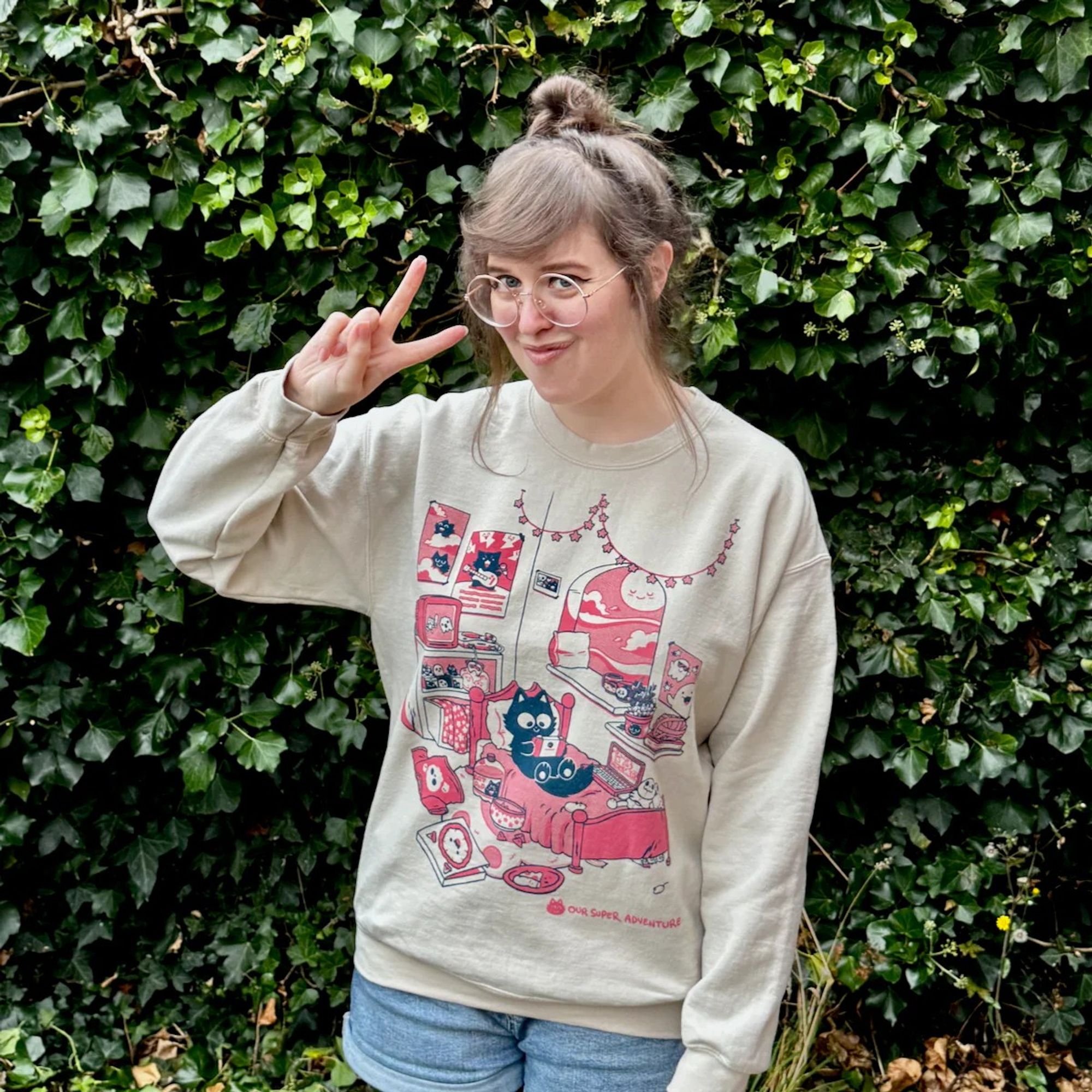 Sarah is posing in the Cat Bedroom sweater, stood in front of a big ivy hedge.