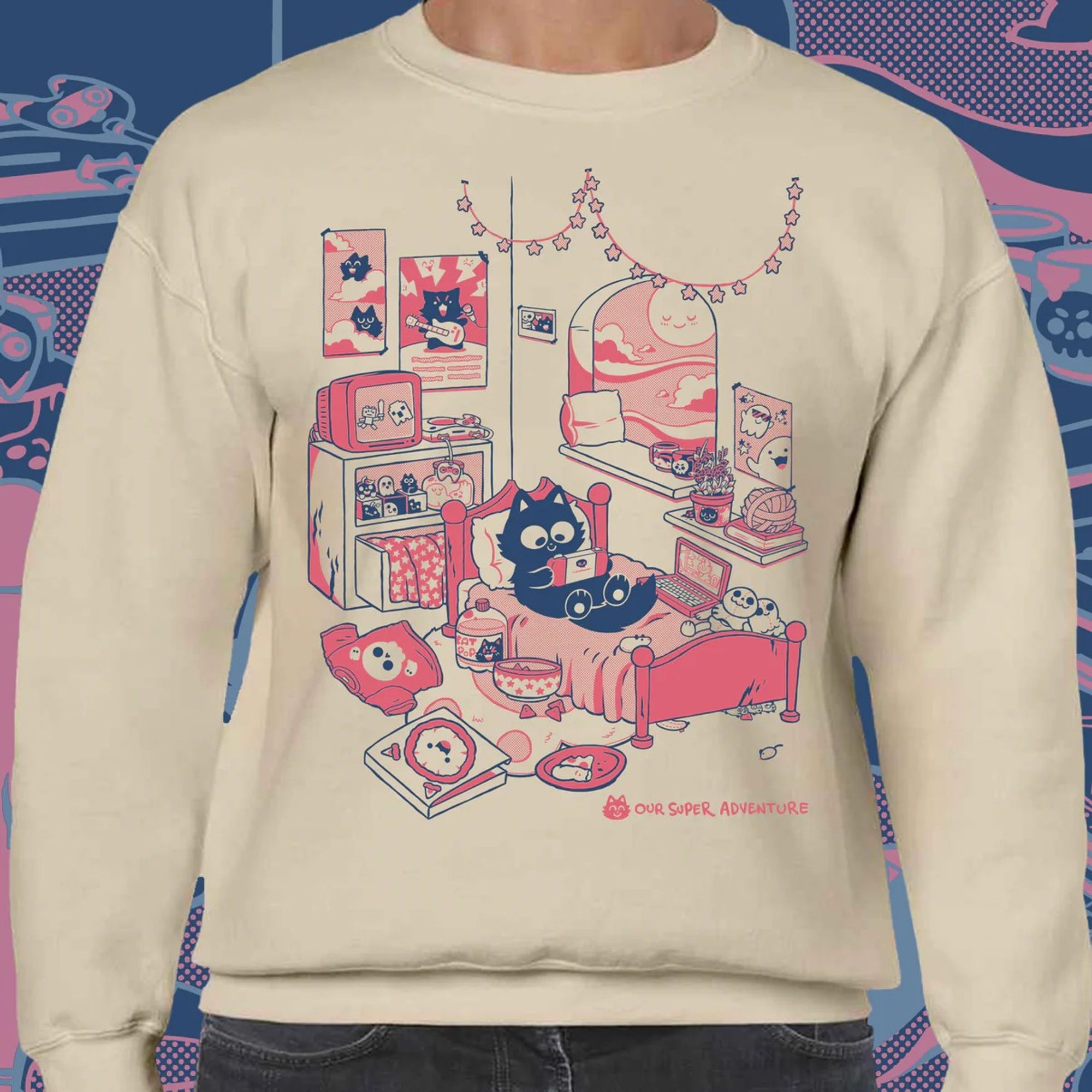 A sweater mock up featuring a design of a fluffy black cat sitting on their bed playing a gaming console, next to a window with a blushing sun and surrounded by plush, snacks, catnip, big yarn ball, posters, mugs, skull t-shirt, empty pizza box. The colours are dark blue and pink ink on a sand coloured background.